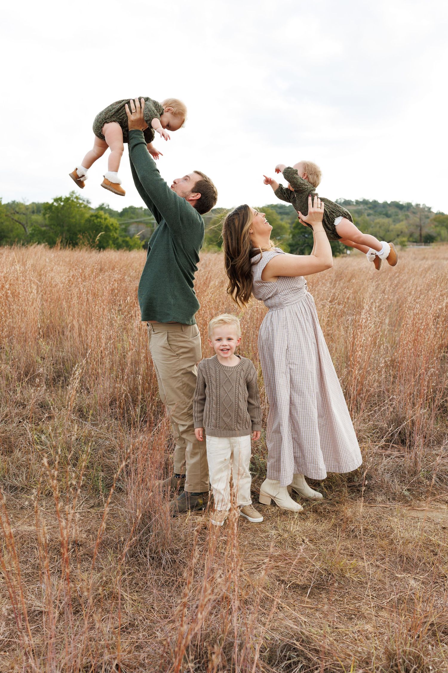 A family in casual attire plays together in a golden autumn field during an outdoor photo session.
