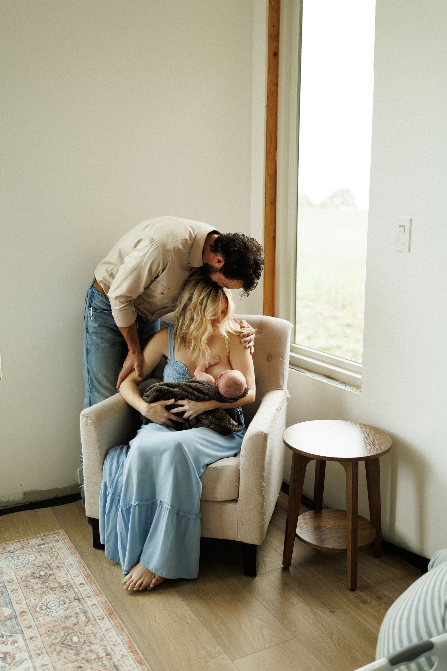 Two people share an intimate moment in a cozy armchair by the window with natural light streaming in.