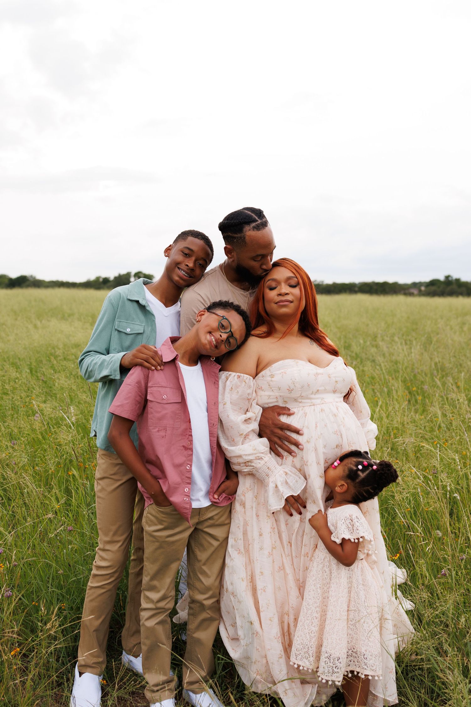 A loving family shares joyful moments together while posing in a sun-lit grassy field.