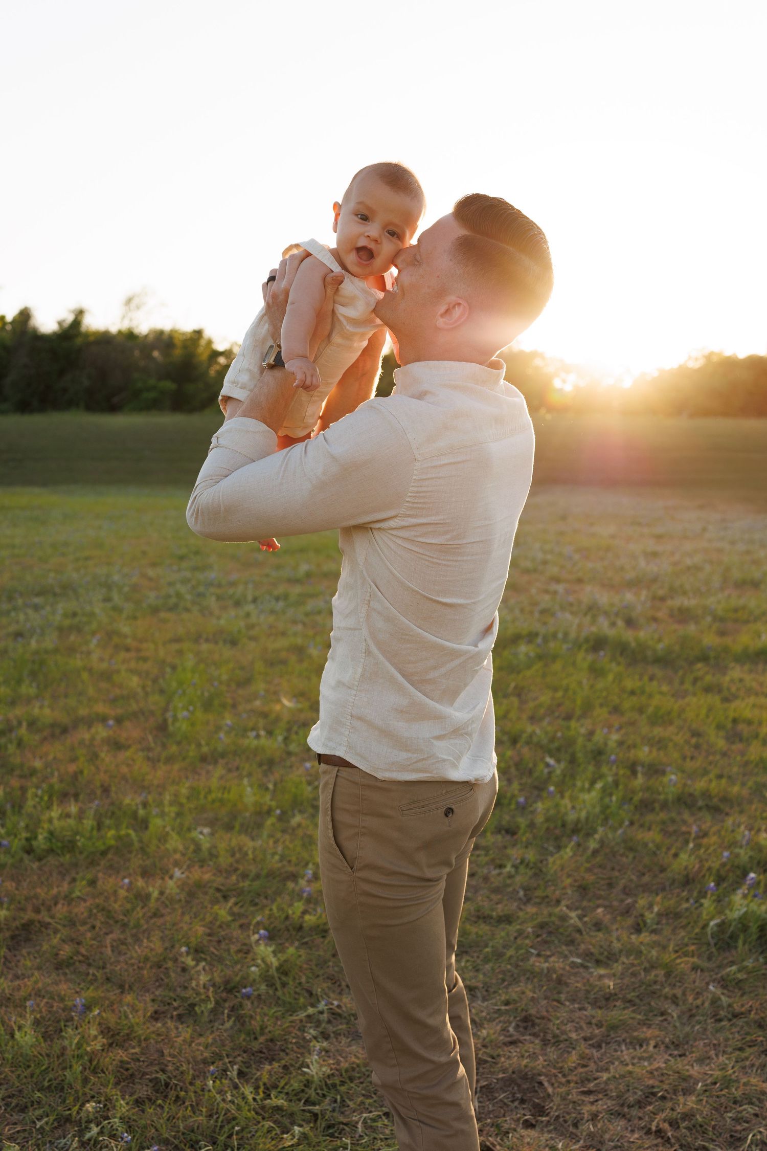 A joyous moment shared between parent and baby in a grassy field at sunset.