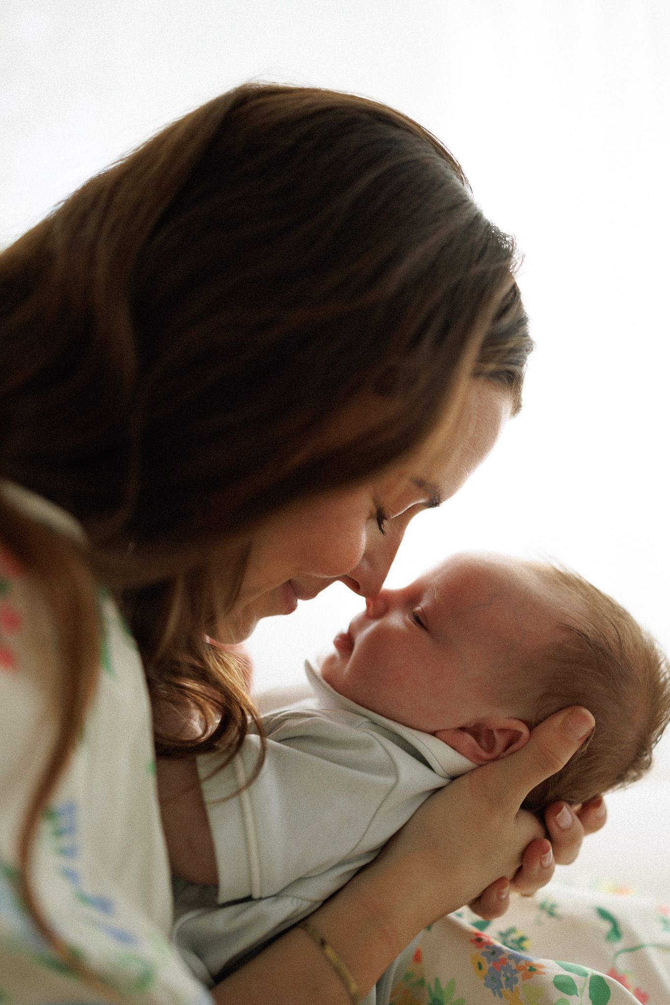 Mother tenderly touching noses with her smiling newborn baby in a bright room.