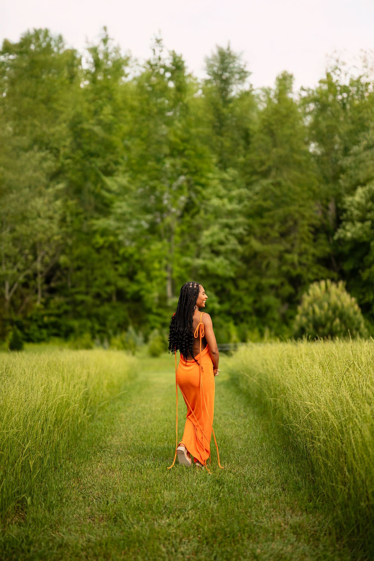 A flowing orange dress contrasts beautifully against tall green grass in a natural outdoor setting.