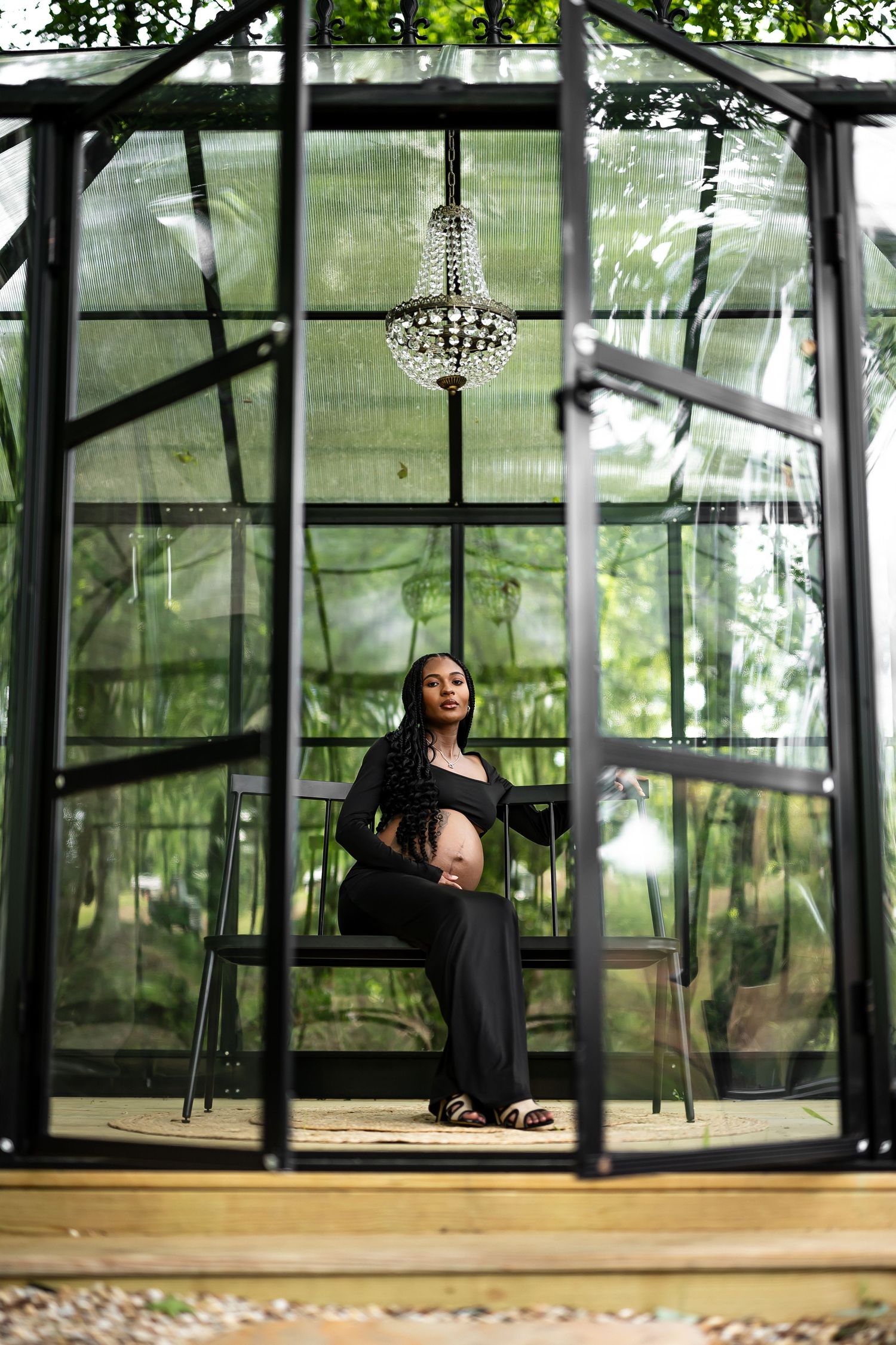 A glass greenhouse structure with wooden floors and a crystal chandelier in a natural outdoor setting.