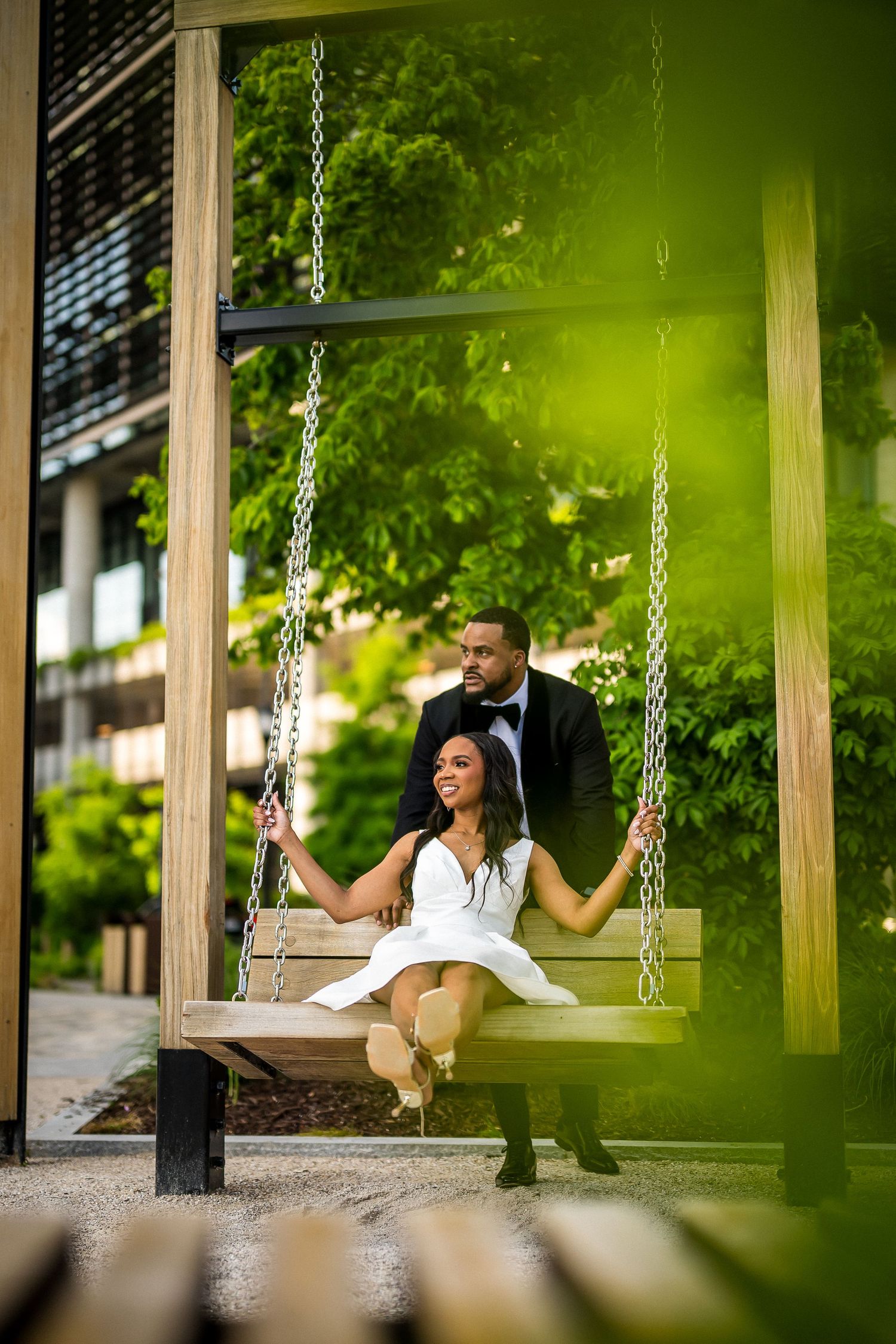 Playful couple enjoys moment on outdoor swings surrounded by green foliage.