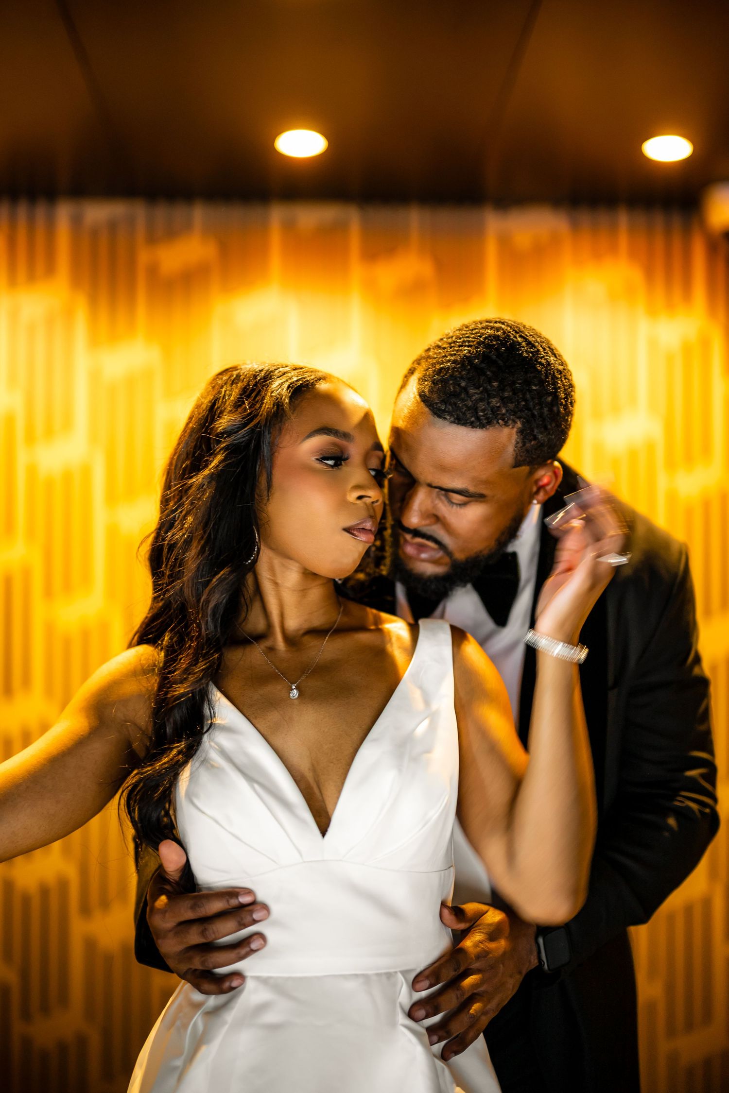 An intimate moment between a couple in formal wear against warm orange lighting.