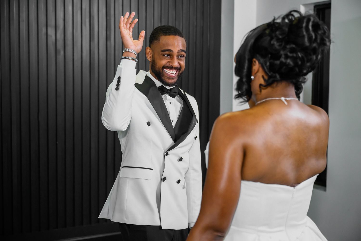 A wedding couple shares joyful moments in black and white formal attire against a dark background.