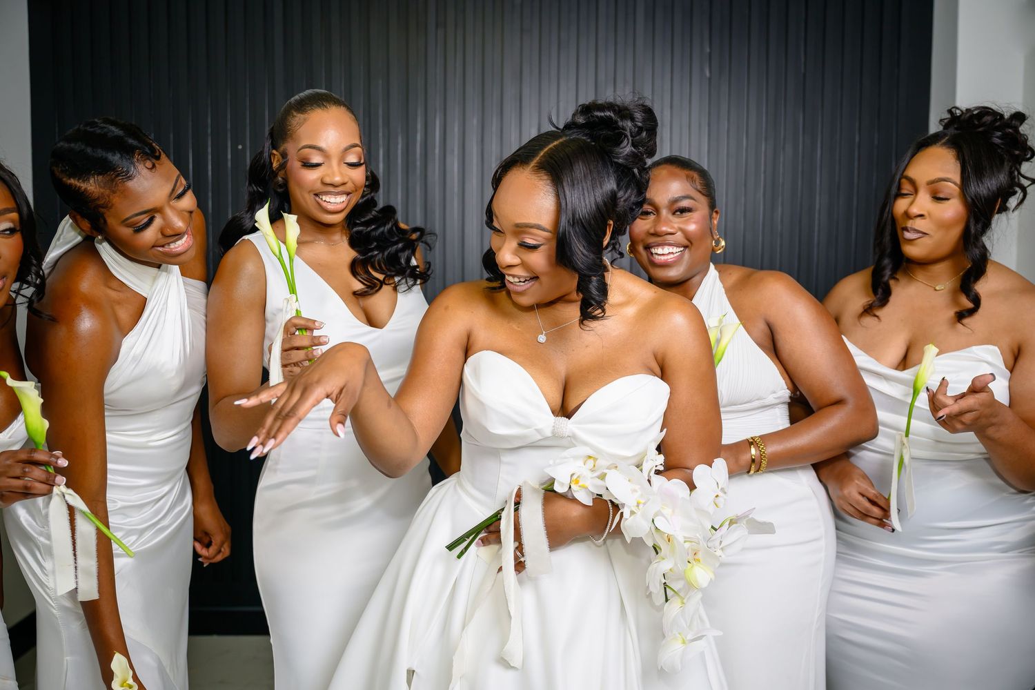 Wedding party members in elegant white dresses share joyful laughter and embraces during a photo session.