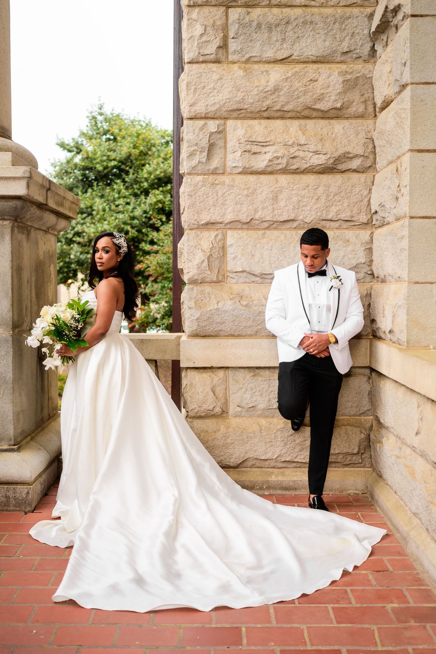 Wedding couple poses dramatically against stone pillars and red brick floor.