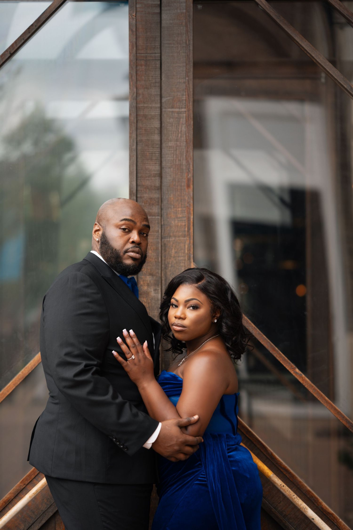 Romantic couple in formal attire poses intimately against wooden beams in an artistic portrait series.