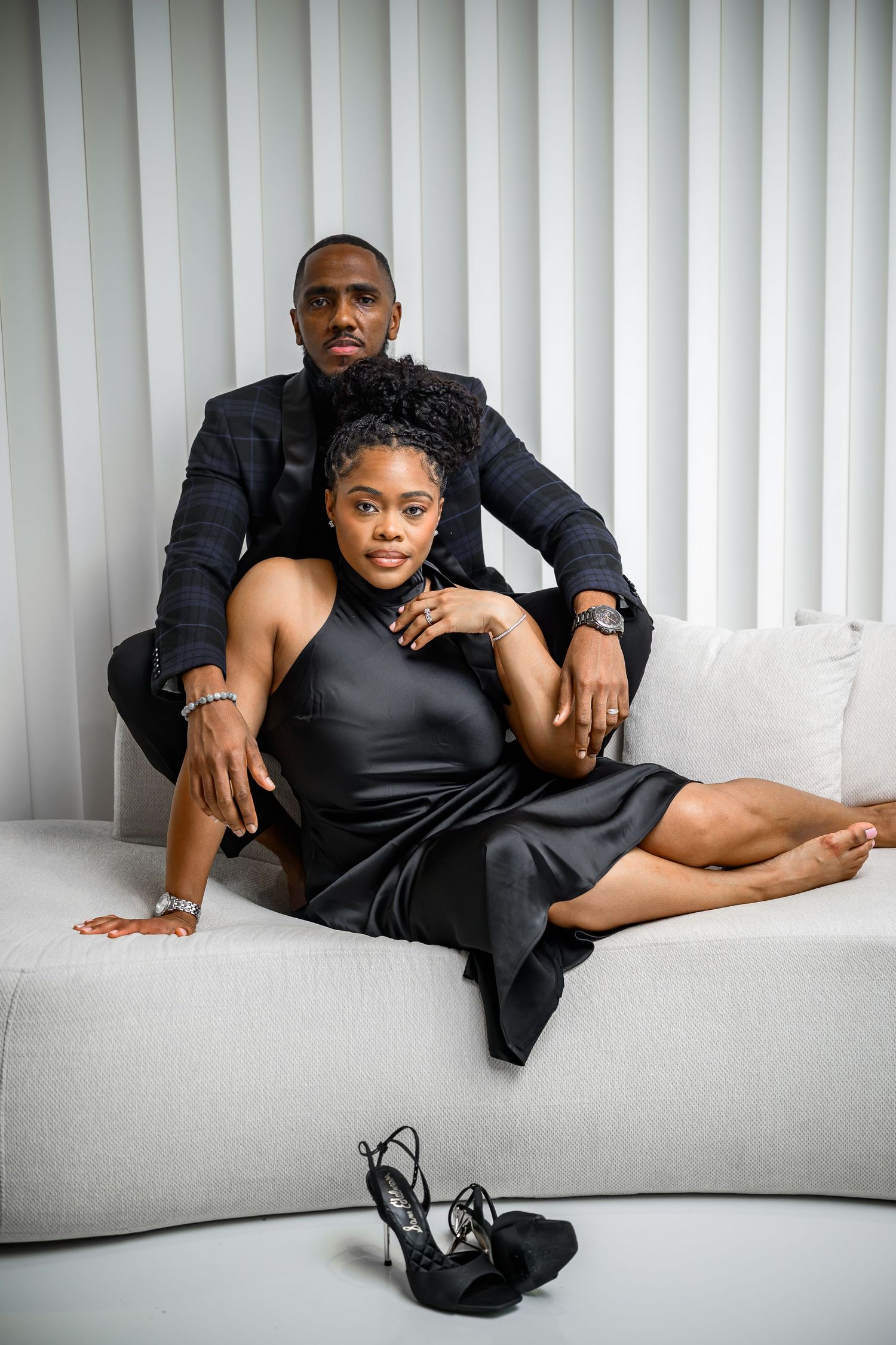 A series of black and white fashion portraits showing a couple lounging on a white couch in dark clothing.