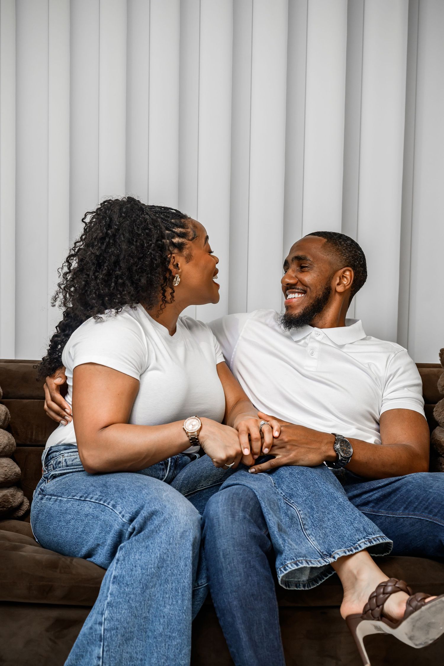 A couple wearing white shirts and jeans laughs together while relaxing on a brown couch in a progression of poses.