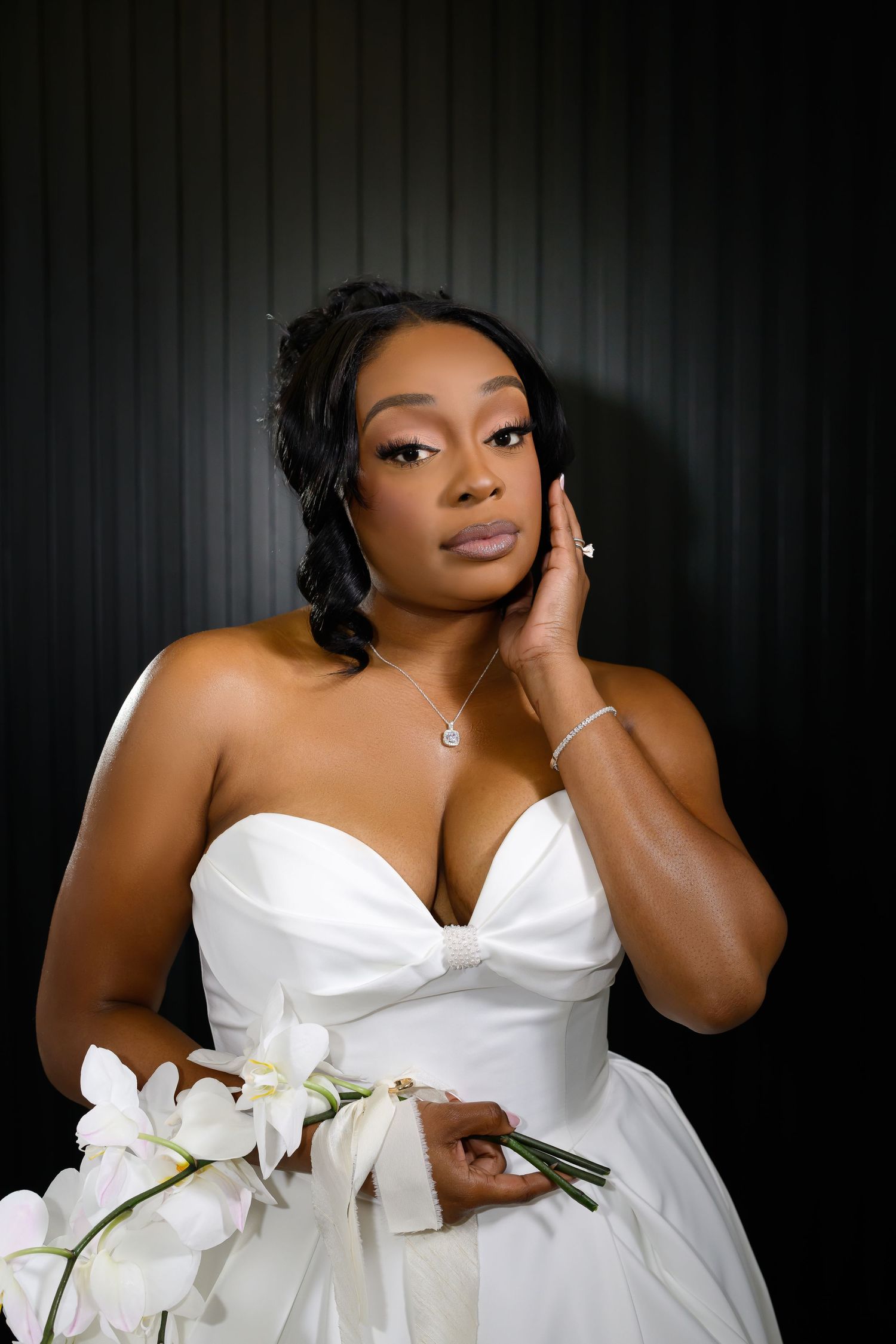 A bridal portrait series showing someone in a white strapless wedding dress posing with white orchids against a dark background.