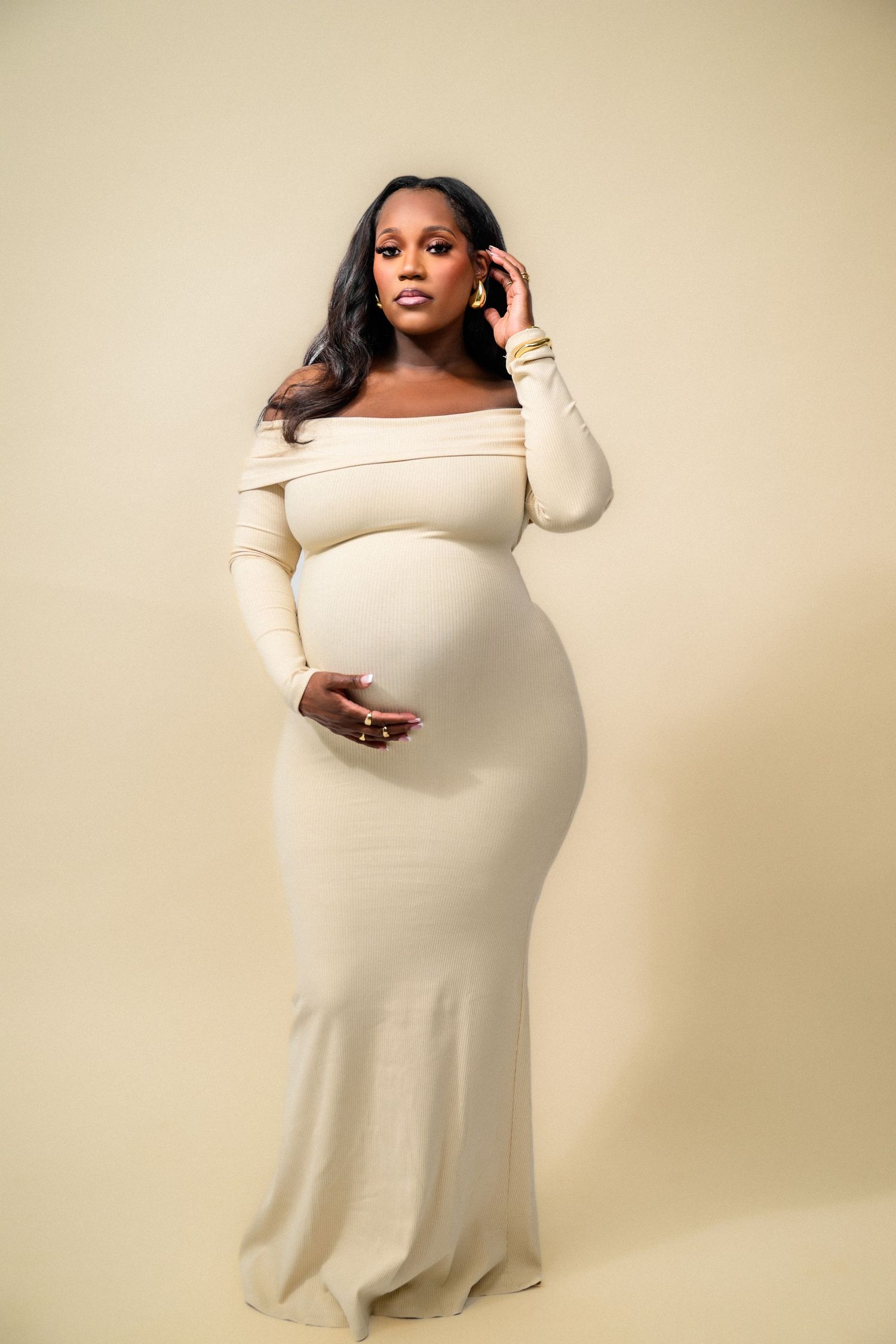 Elegant maternity portraits in cream off-shoulder dress against neutral backdrop.