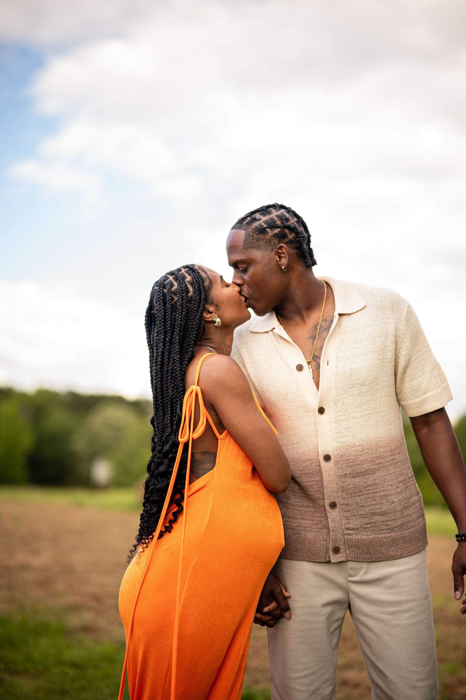 A romantic moment shared between a couple wearing orange and beige against a cloudy sky.