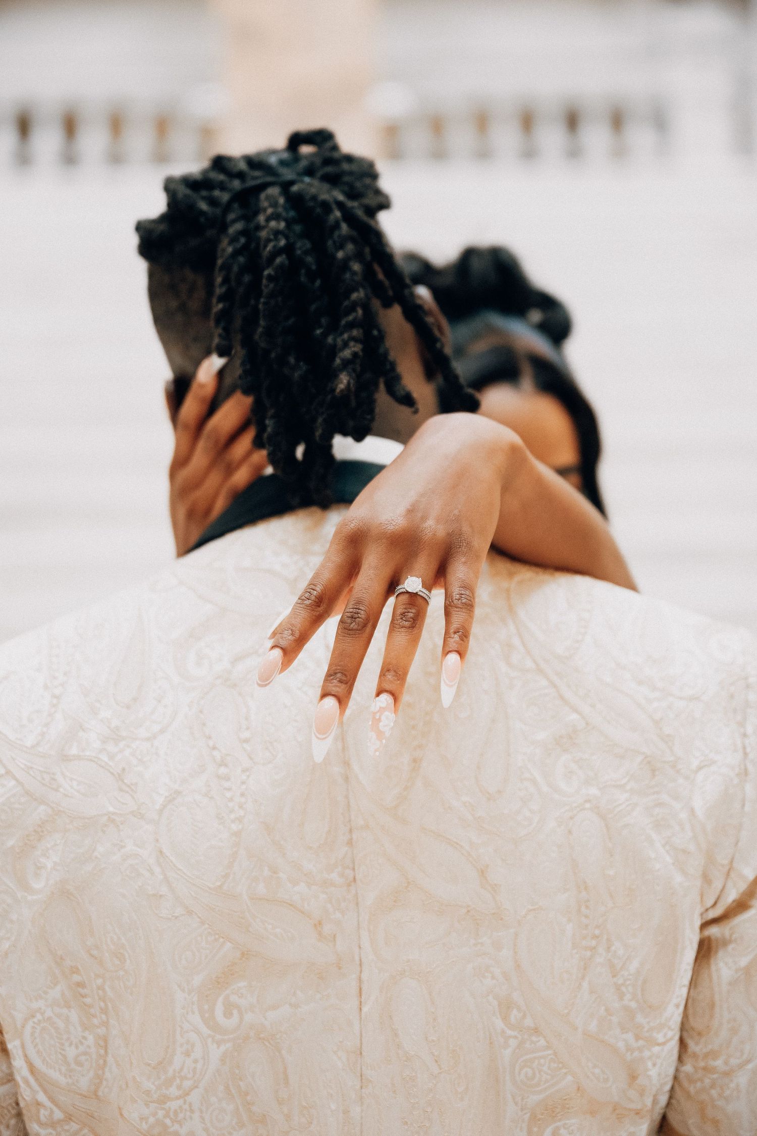 Close-up of hands showing off an engagement ring against a white lace dress.