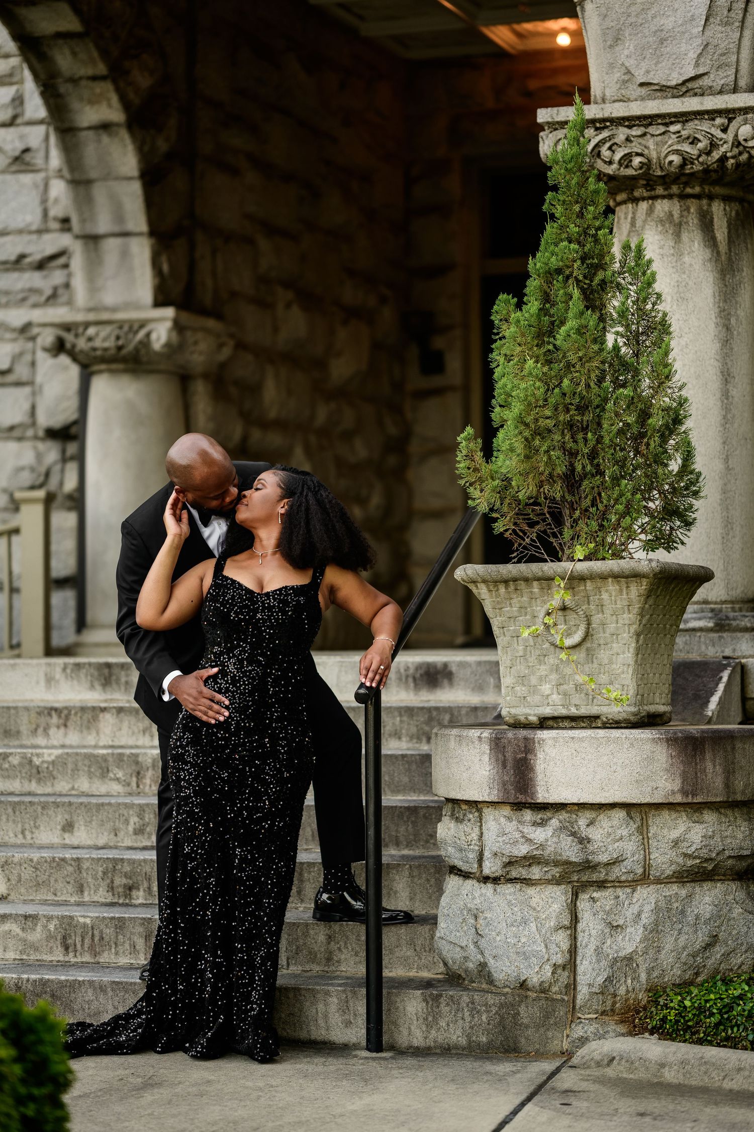 Elegant couple in formal attire poses on stone steps during a romantic photoshoot.