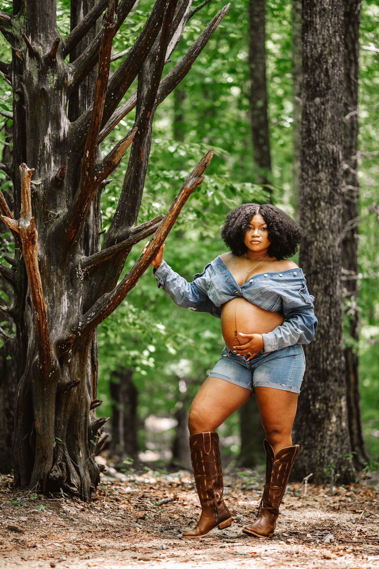 Forest maternity session featuring casual denim look and brown leather boots among tall trees.