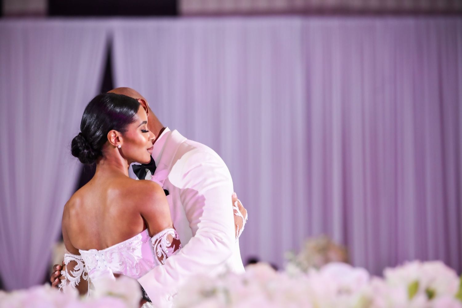 Elegant wedding celebration with couples dancing under purple mood lighting.