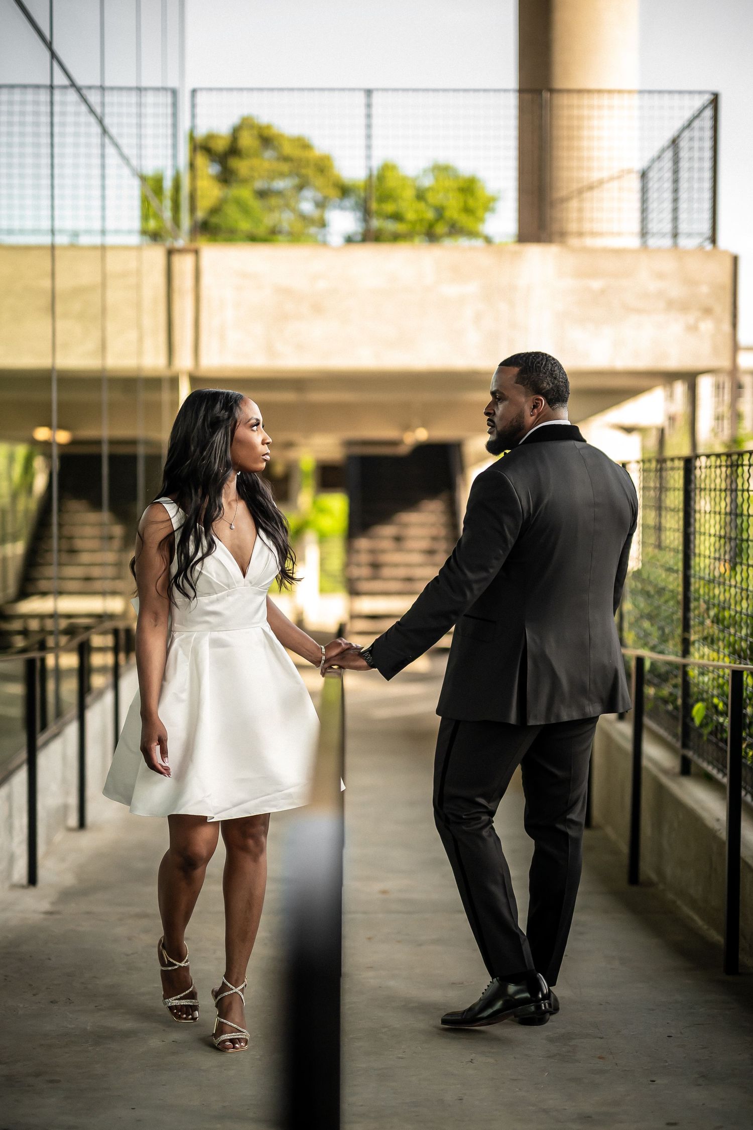 A couple in formal attire shares a romantic moment on an outdoor walkway.