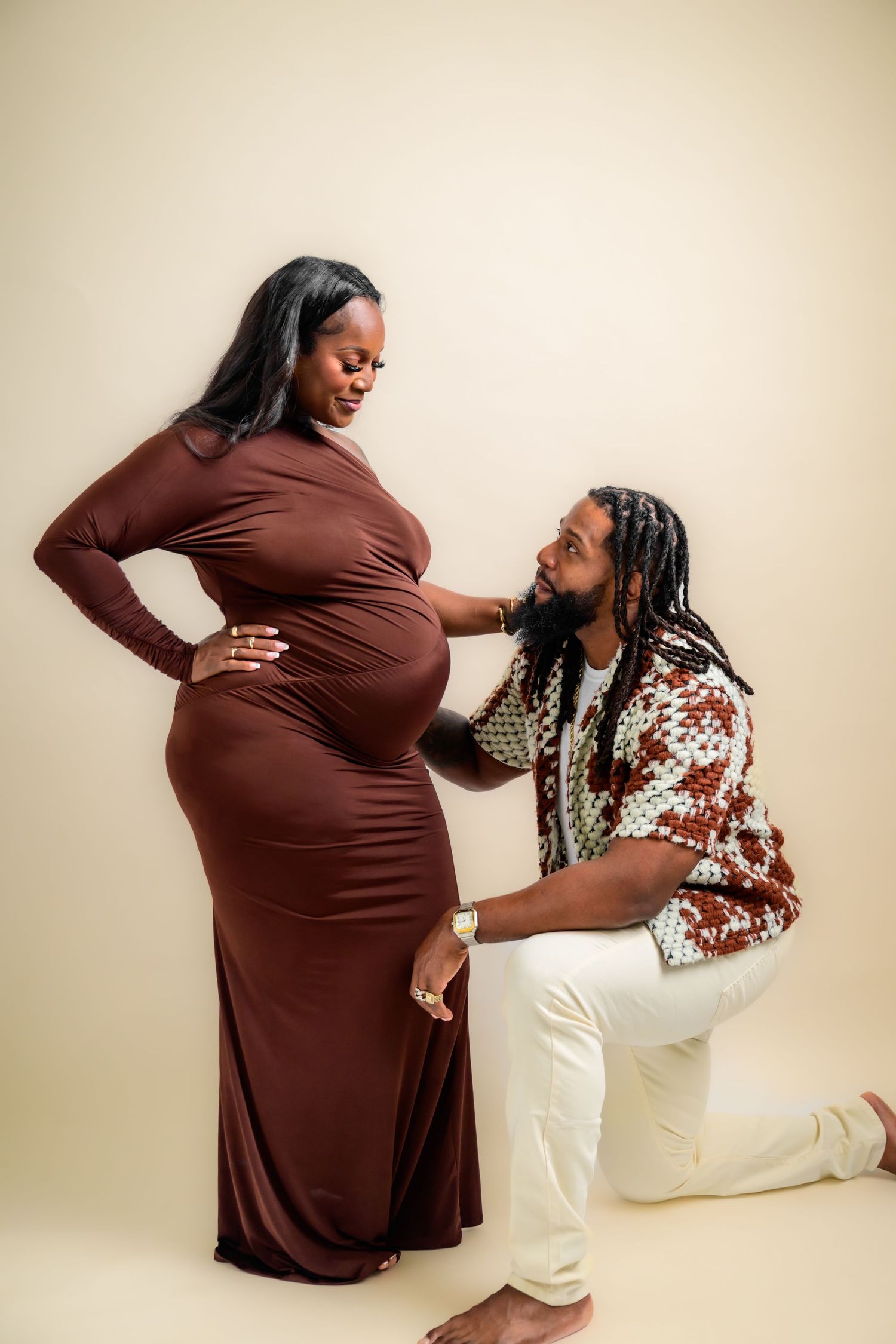 Creative pregnancy photoshoot with couple in coordinated brown and white outfits.