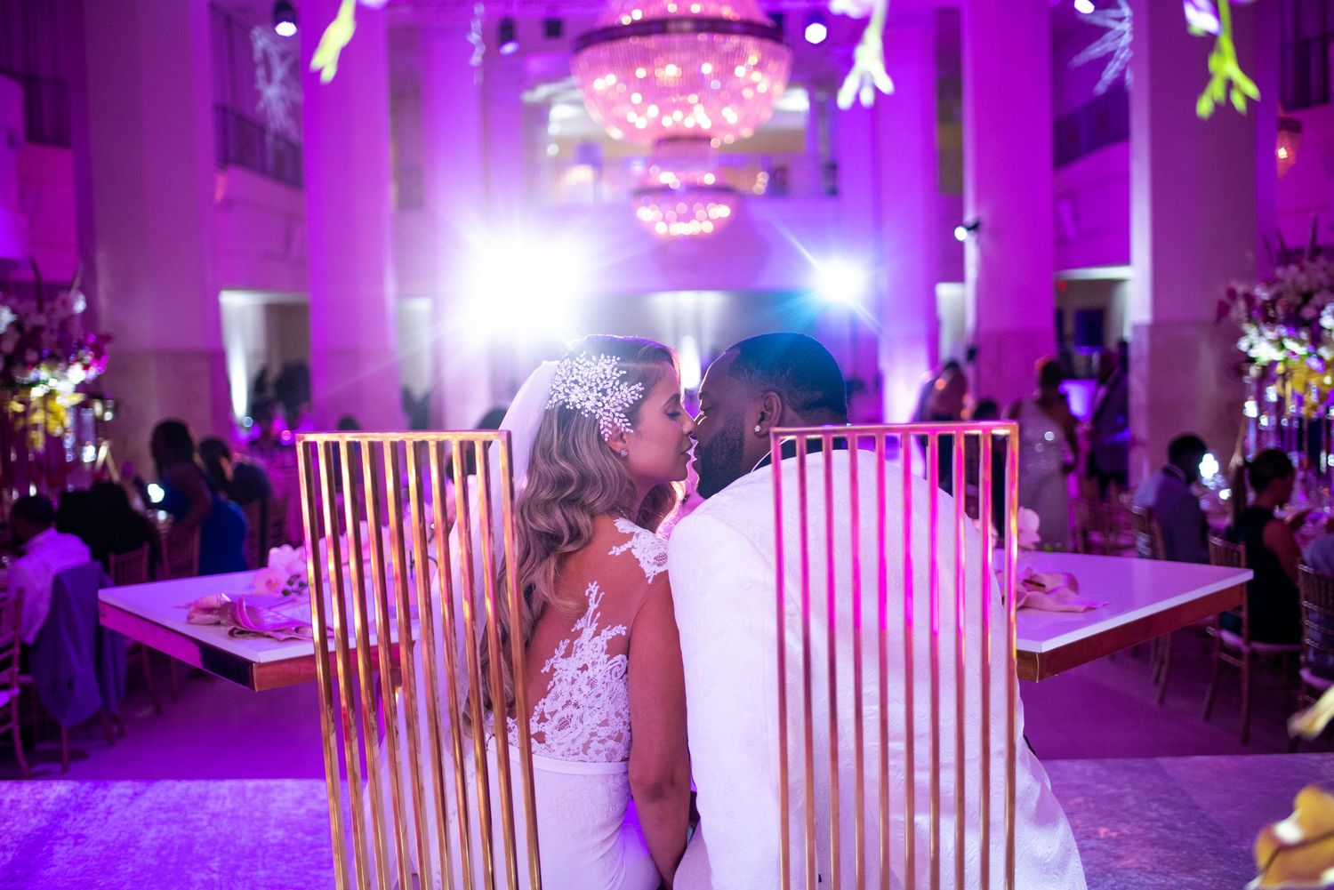 Reception venue illuminated in vibrant purple lighting with white chairs.