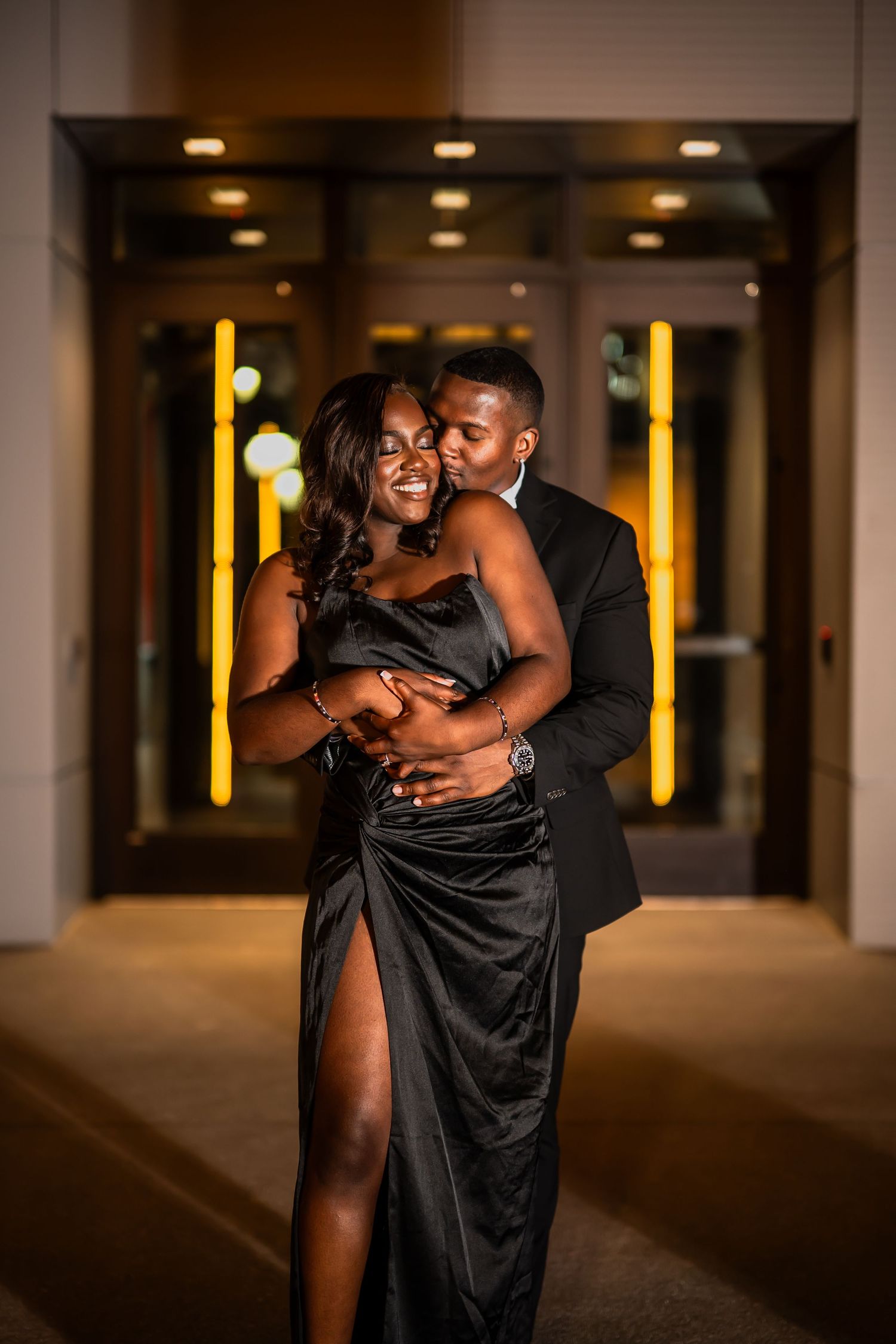Romantic evening portrait in formal attire with illuminated yellow lights in background.
