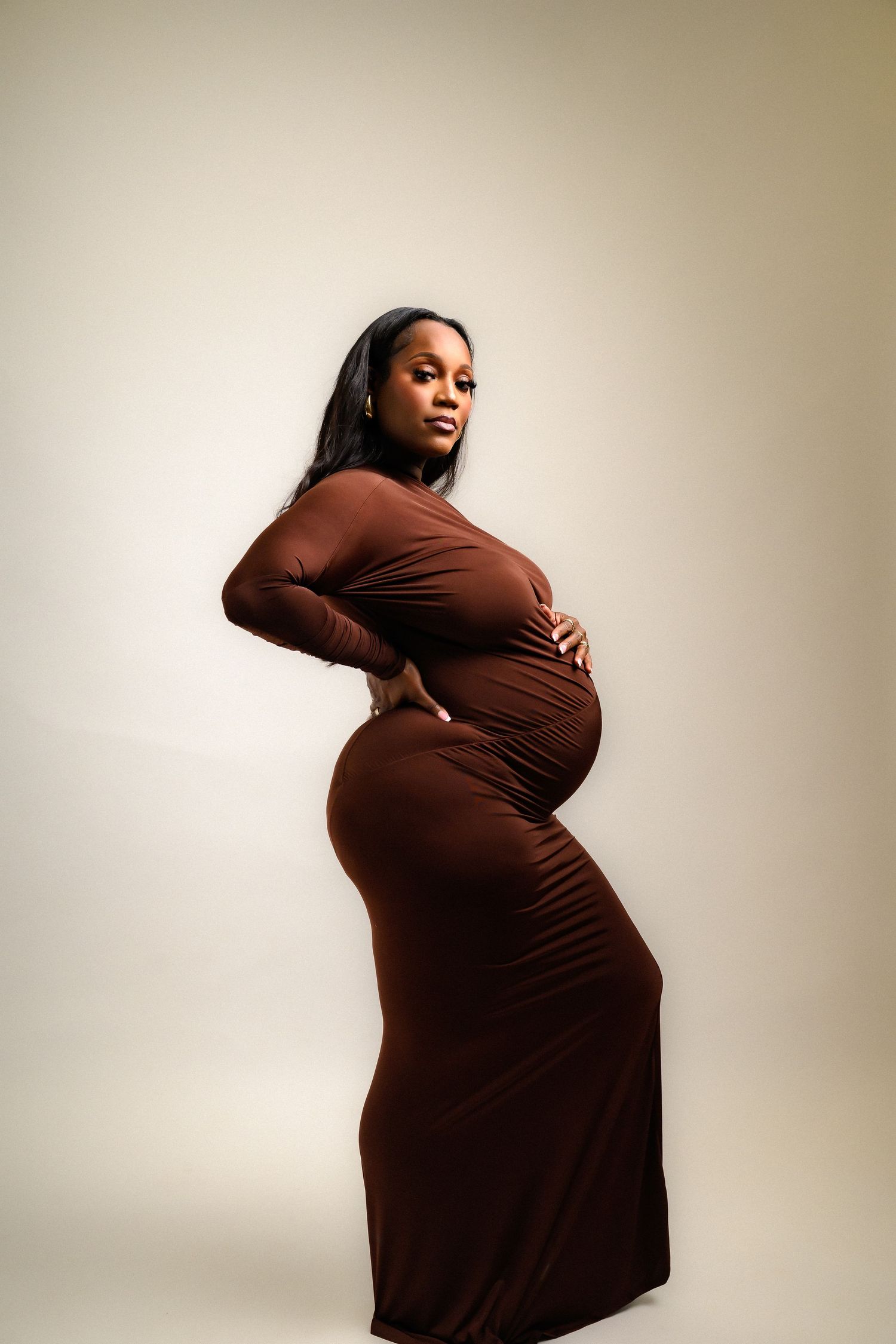 Elegant maternity portraits highlighting pregnancy in fitted brown dress.
