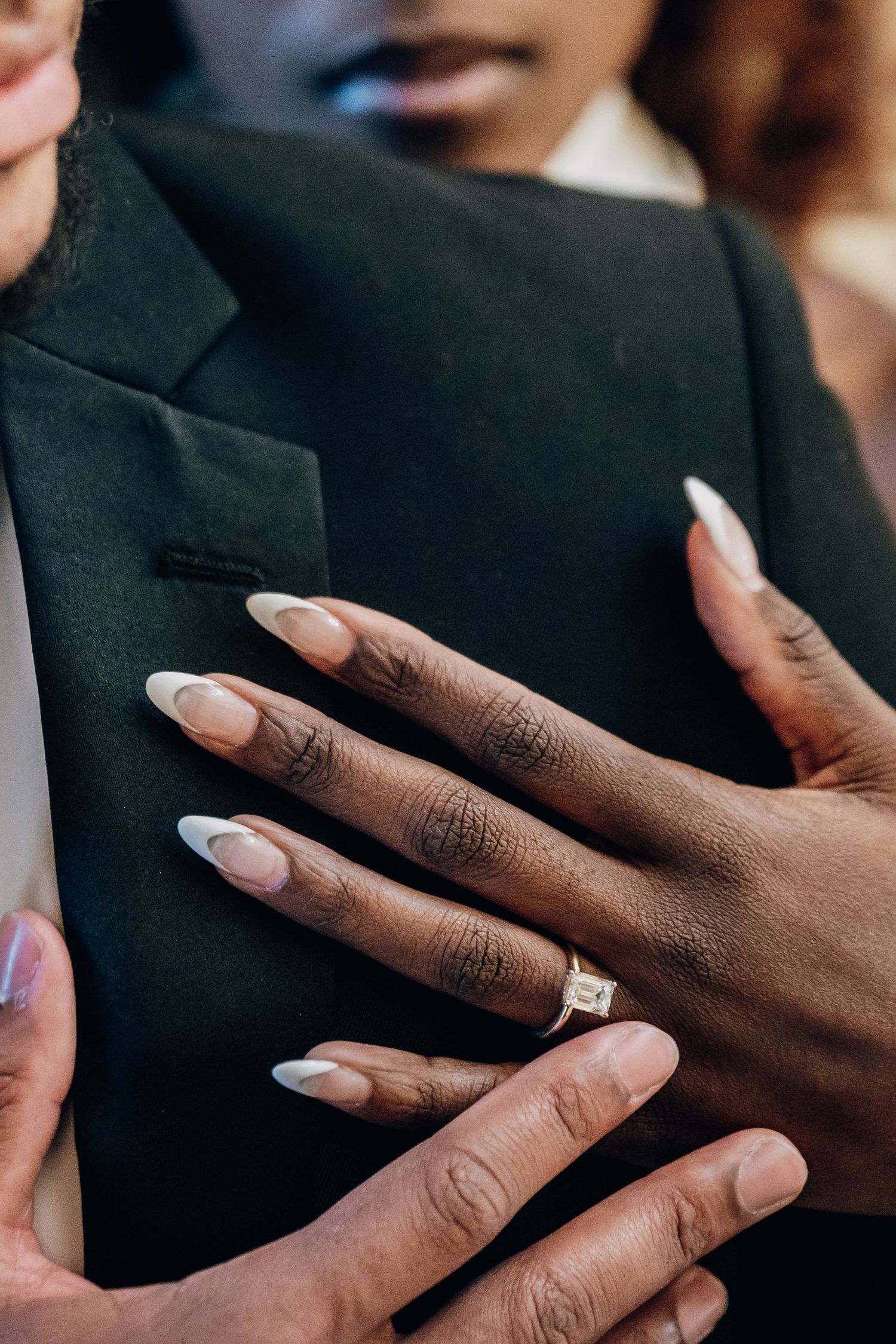 Close-up of hands with elegant white manicured nails against a dark background.