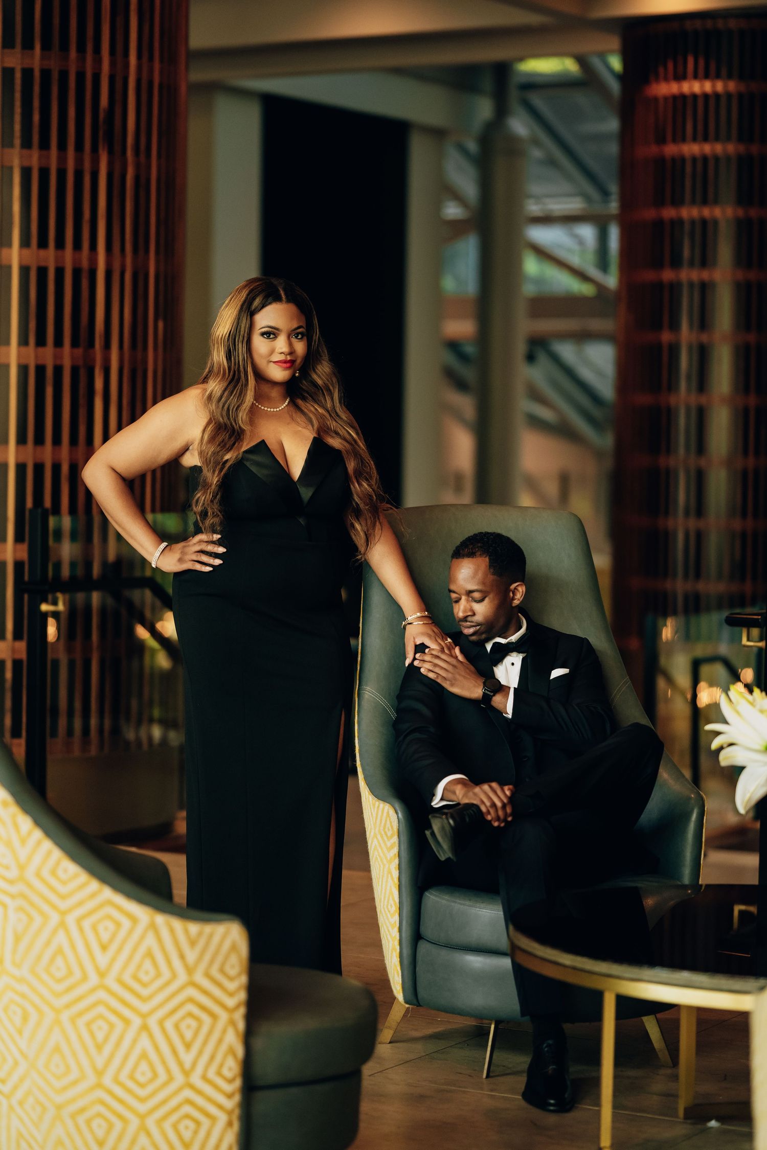Couple in formal black attire poses intimately in modern lounge with geometric decor.