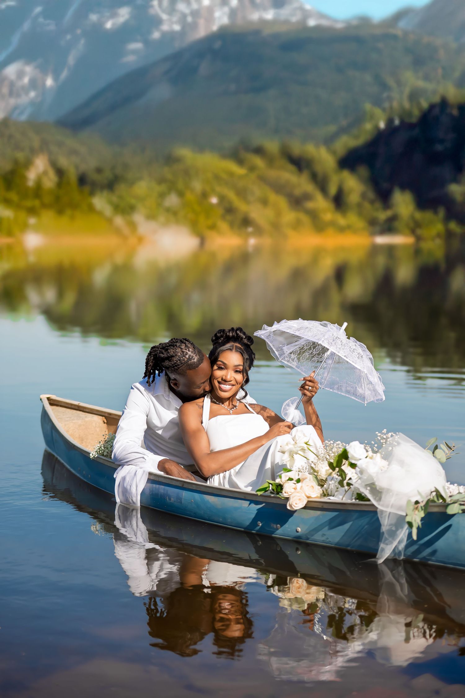 Romantic couple in wedding attire share intimate moment in canoe on mountain lake with parasol.