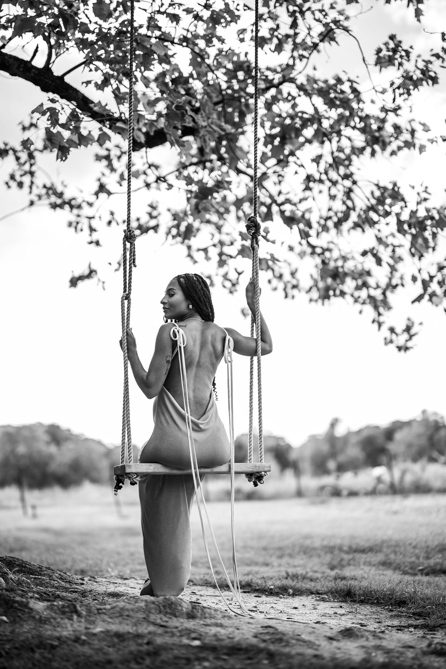 A dreamy black and white series showing someone on a rustic wooden swing under tree branches.