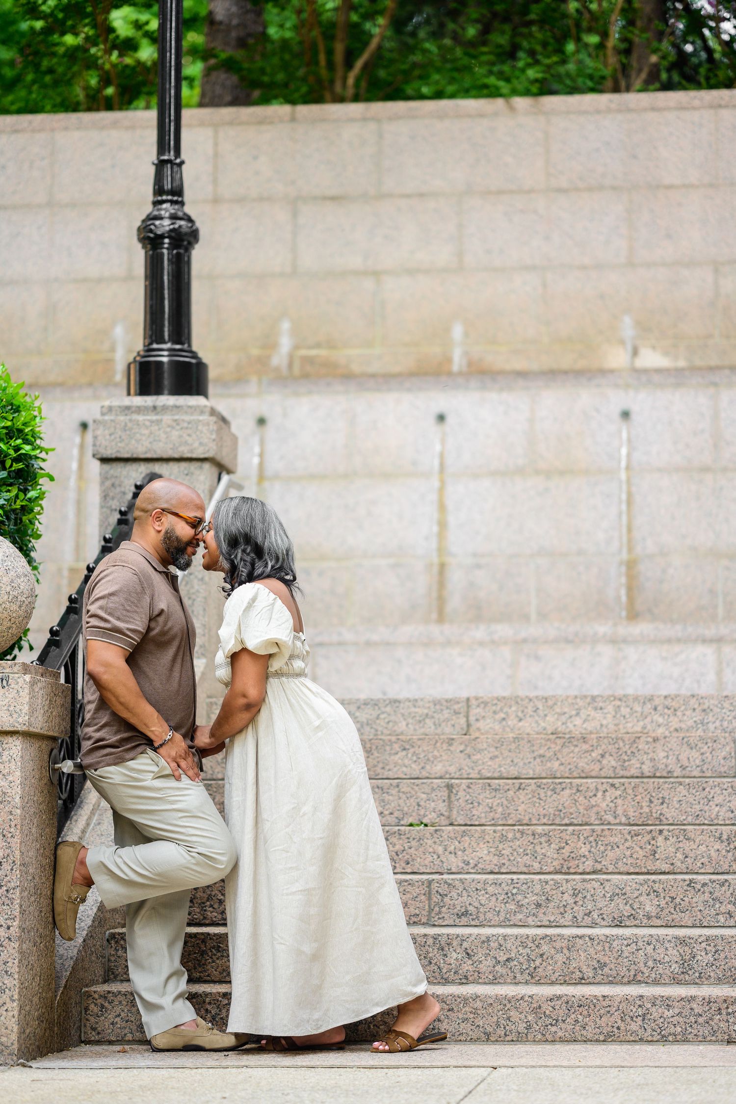 Couple sitting and embracing on stone steps near decorative lamp posts.