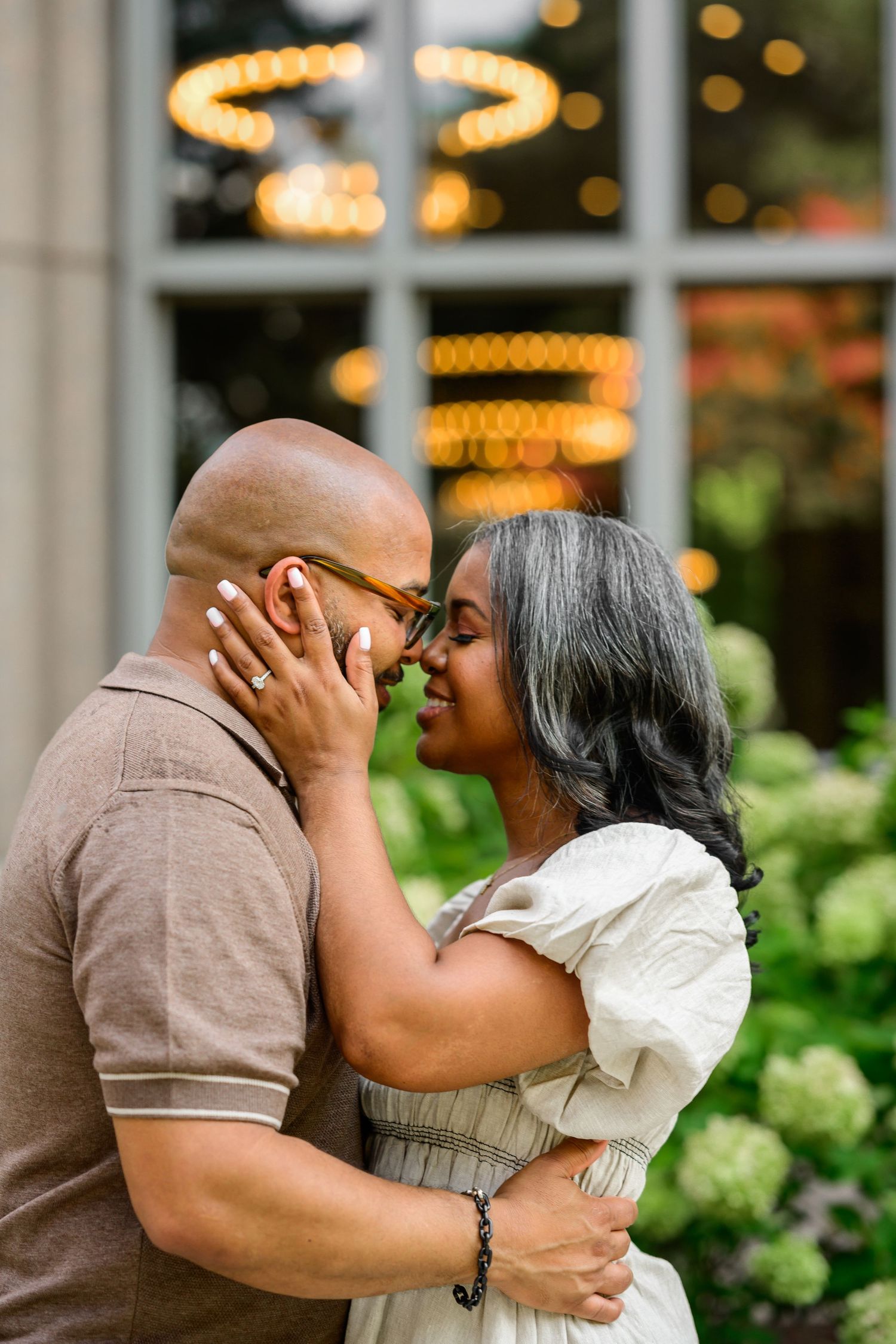 Romantic couple sharing affectionate moments in front of a building with twinkling lights.