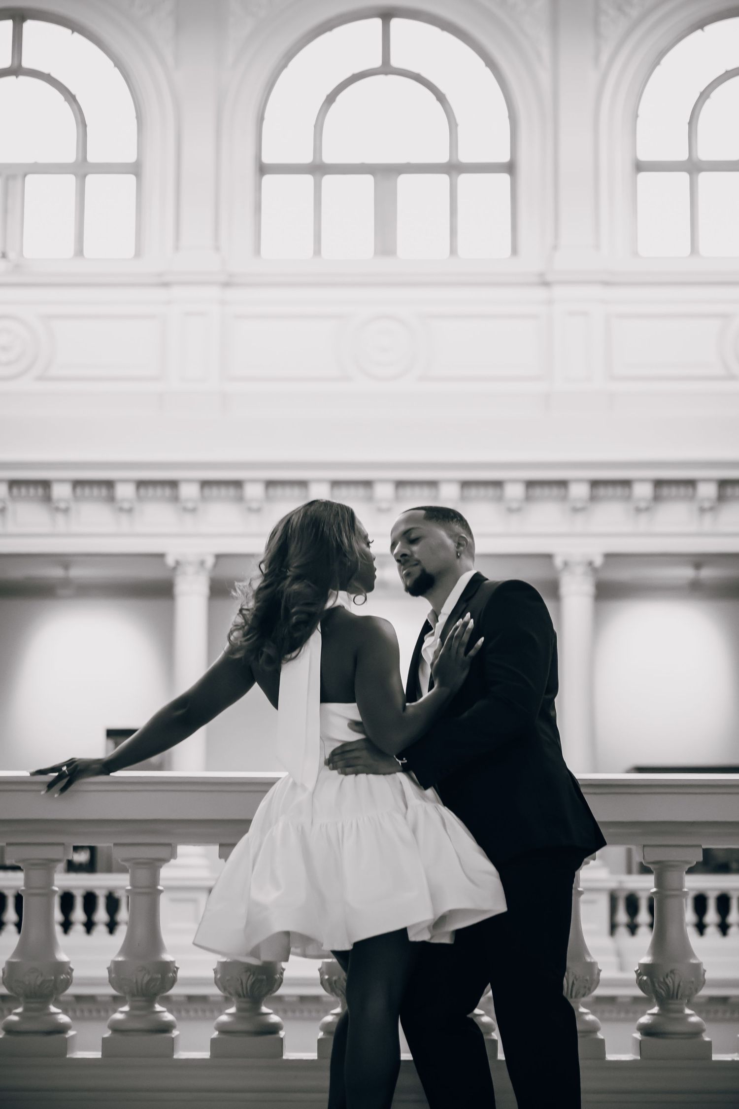 Elegant couple dancing in a grand white hall with classical architecture.