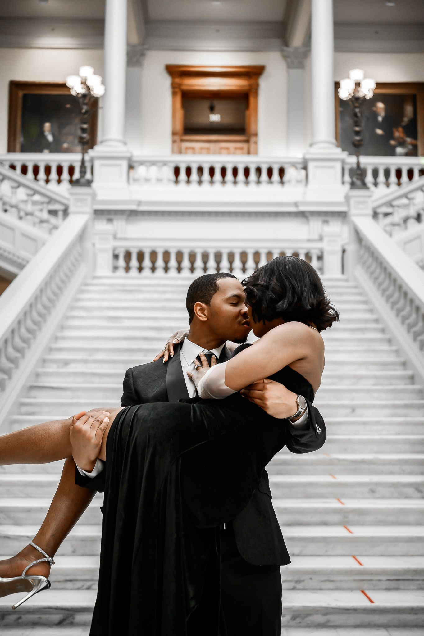 Romantic dip pose on grand marble staircase with classical architecture background.