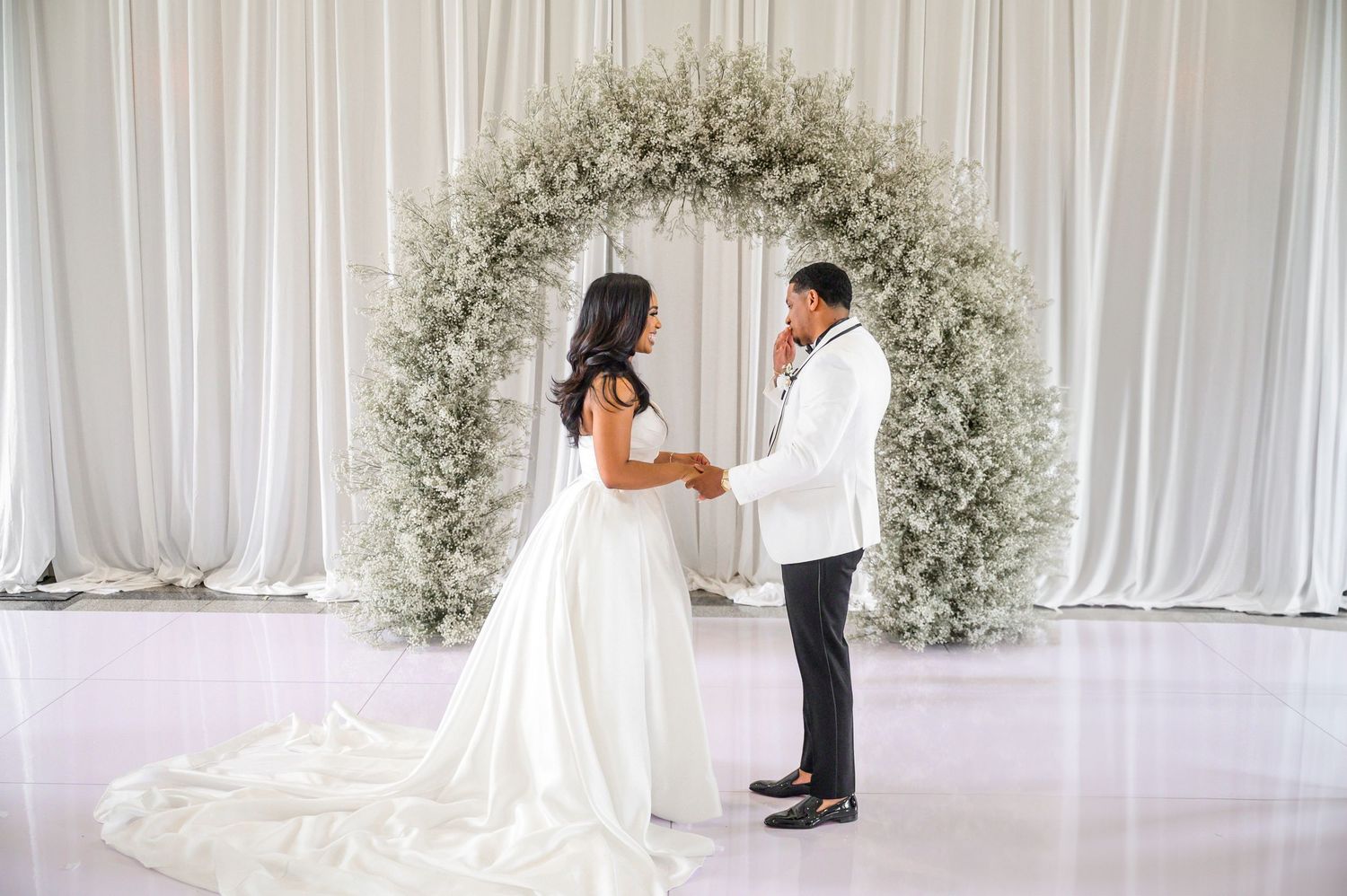 Wedding ceremony space decorated with white drapes and a floral arch made of baby's breath.