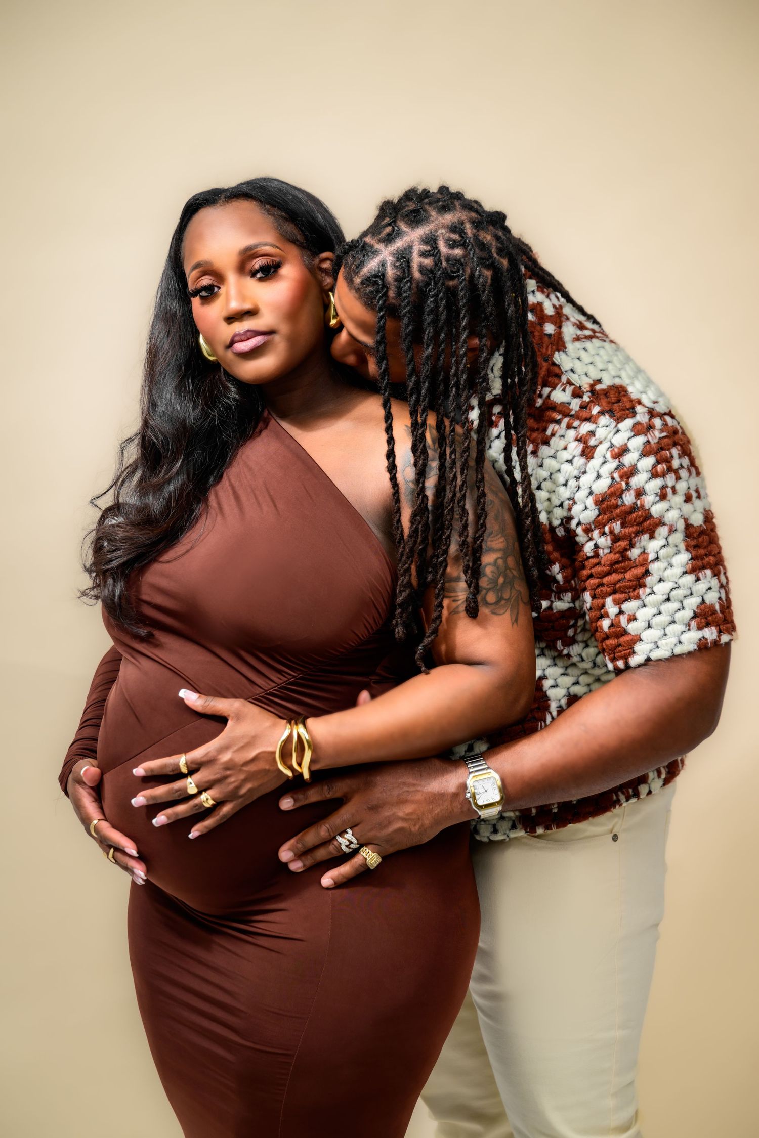 Loving maternity portraits with couple in brown dress and patterned shirt against neutral background.