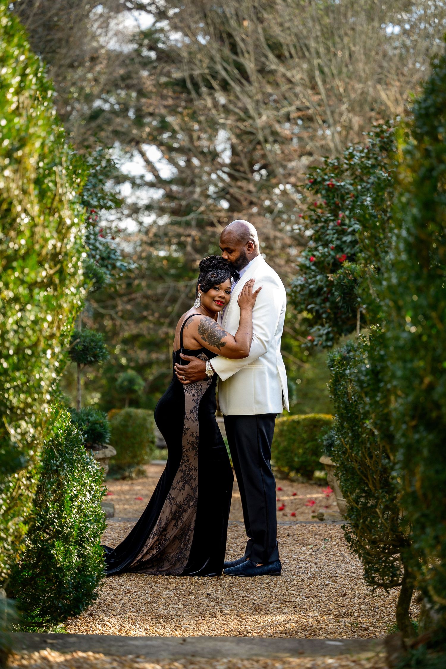 A couple shares an intimate dance moment together on a gravel path surrounded by greenery in a garden setting.
