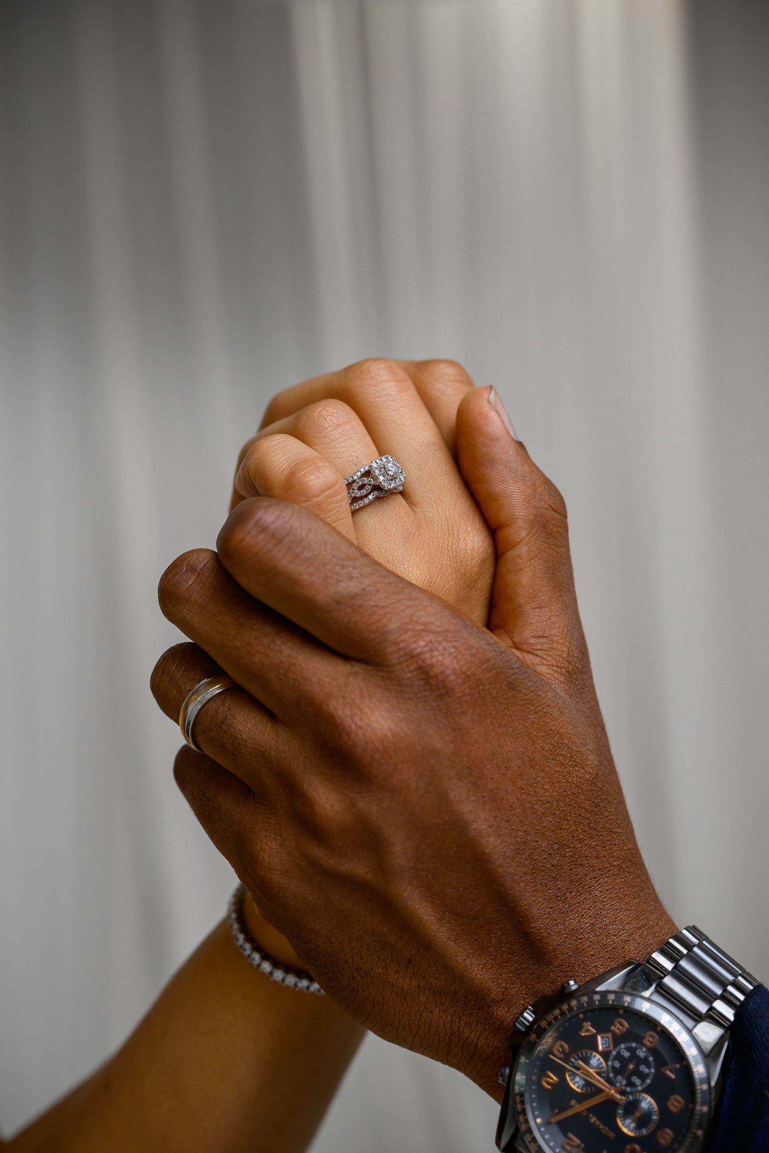 Two hands of different skin tones clasped together in unity against a blurred background with one wearing a watch.