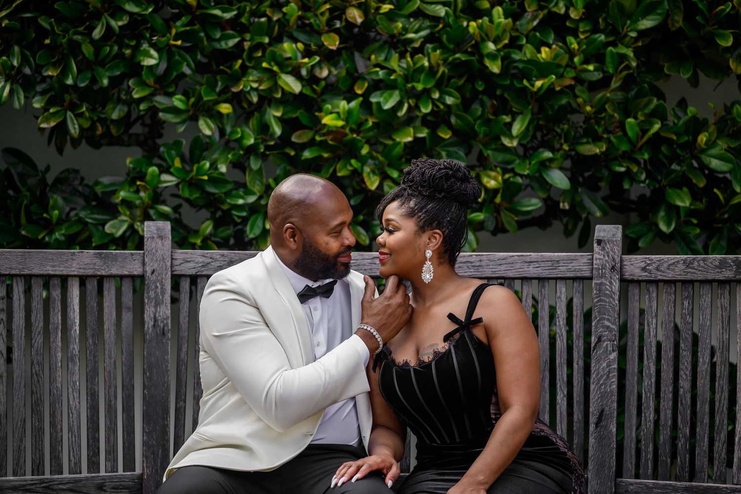 A romantic couple shares intimate moments in an outdoor garden setting with a wooden fence backdrop.