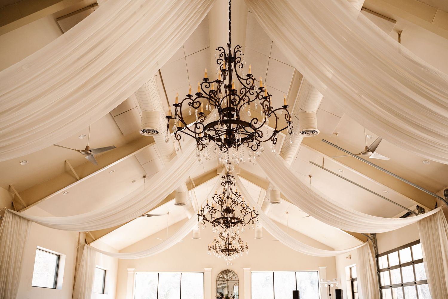 Elegant reception hall with white fabric draped ceiling and crystal chandeliers creating romantic ambiance.