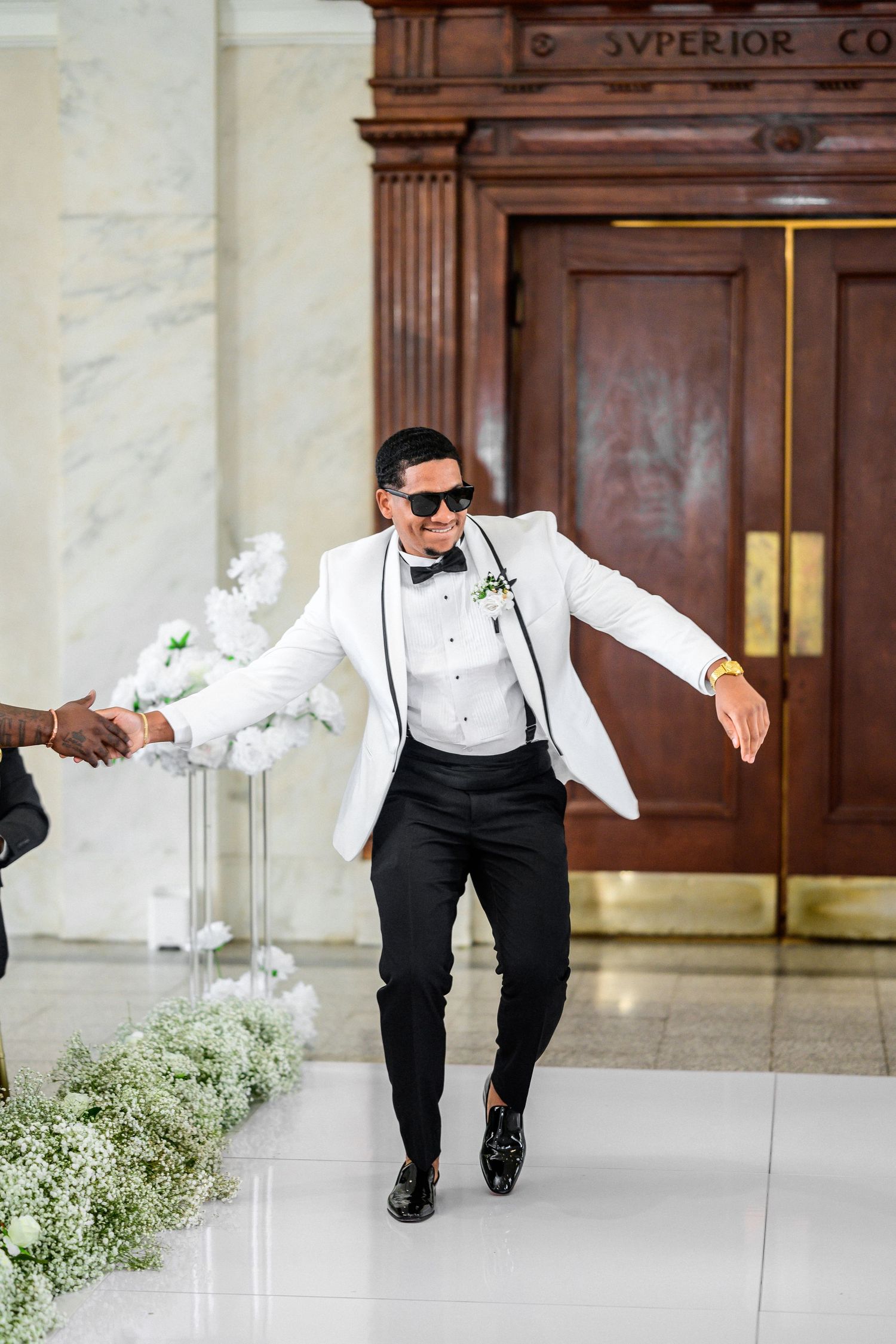 Wedding party member in white tuxedo jacket and black pants dances in a courthouse setting.