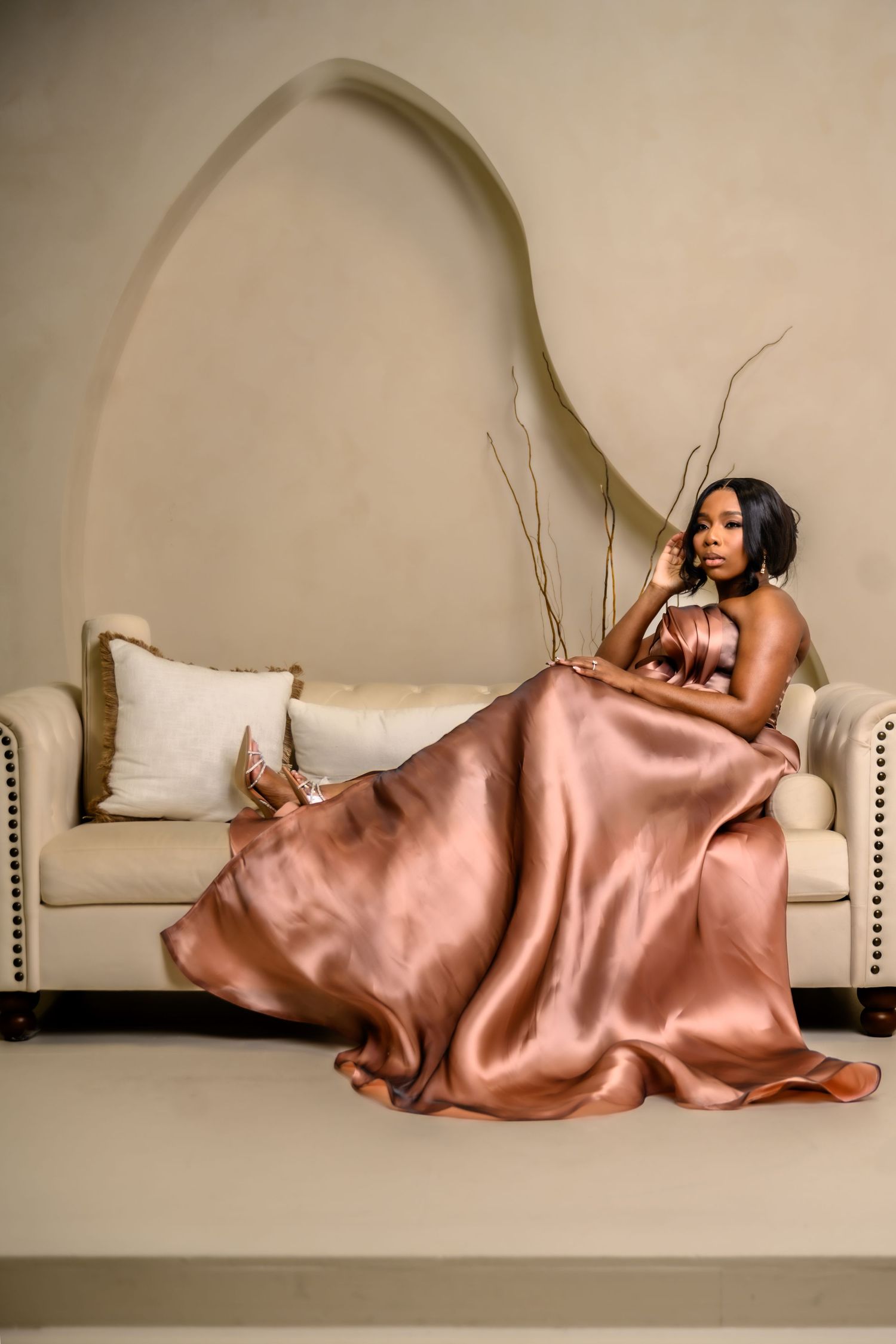 Fashion portrait on a curved white bench featuring flowing rose gold silk fabric.