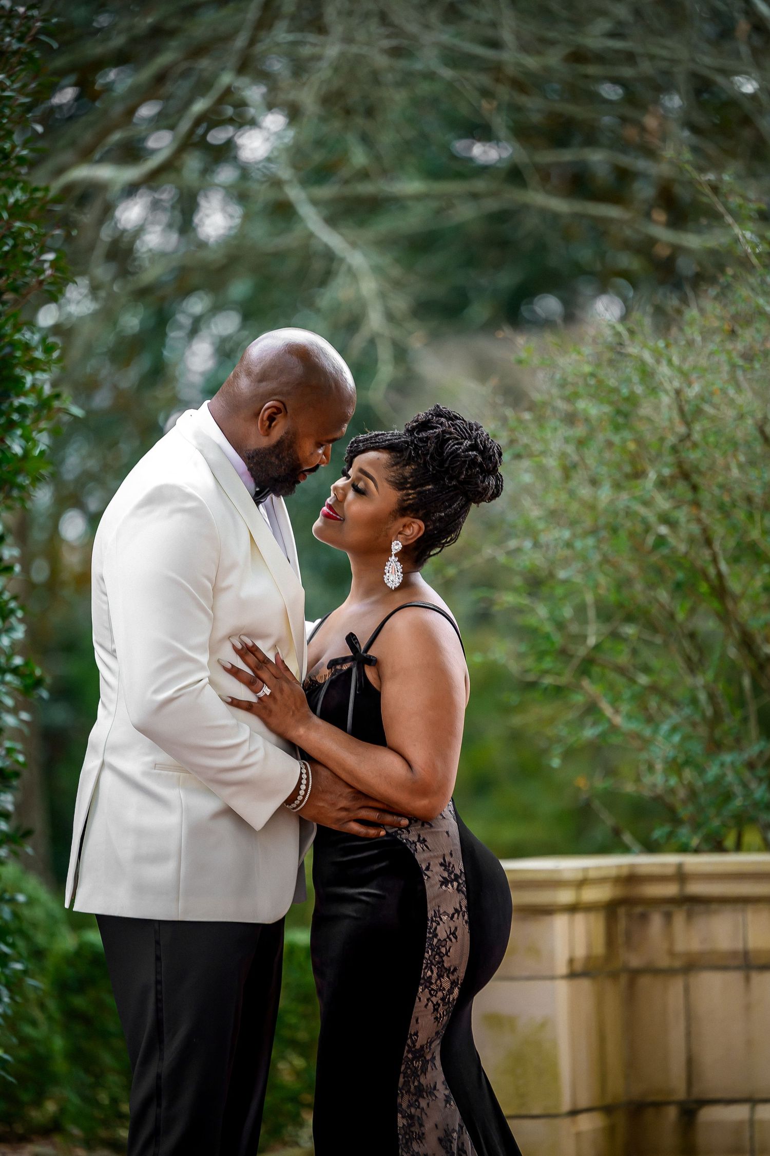 A couple shares an intimate moment together in an outdoor garden setting wearing formal attire.