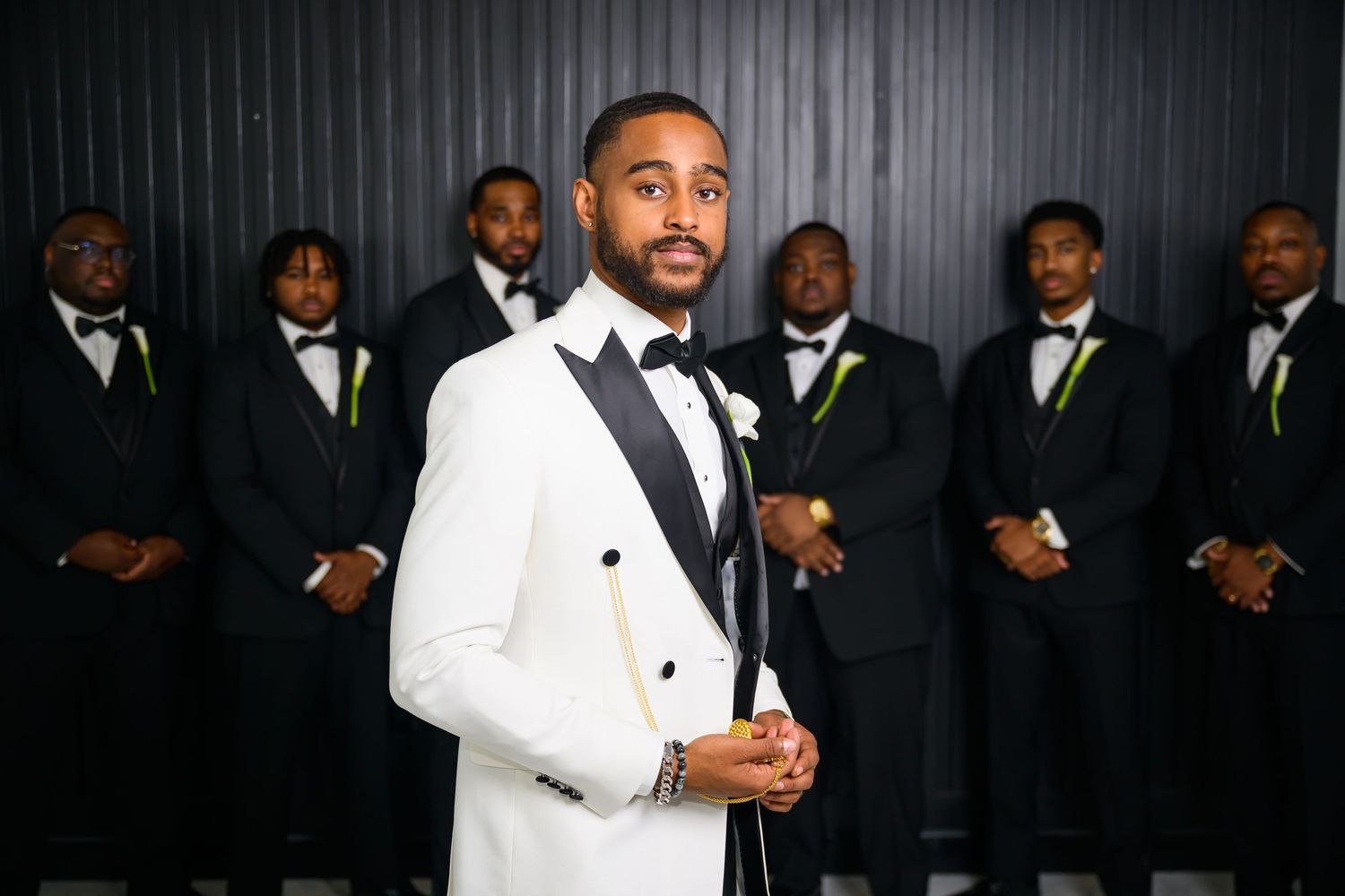 A wedding party in formal attire poses in front of a dark backdrop with groomsmen wearing black suits and lime green ties.