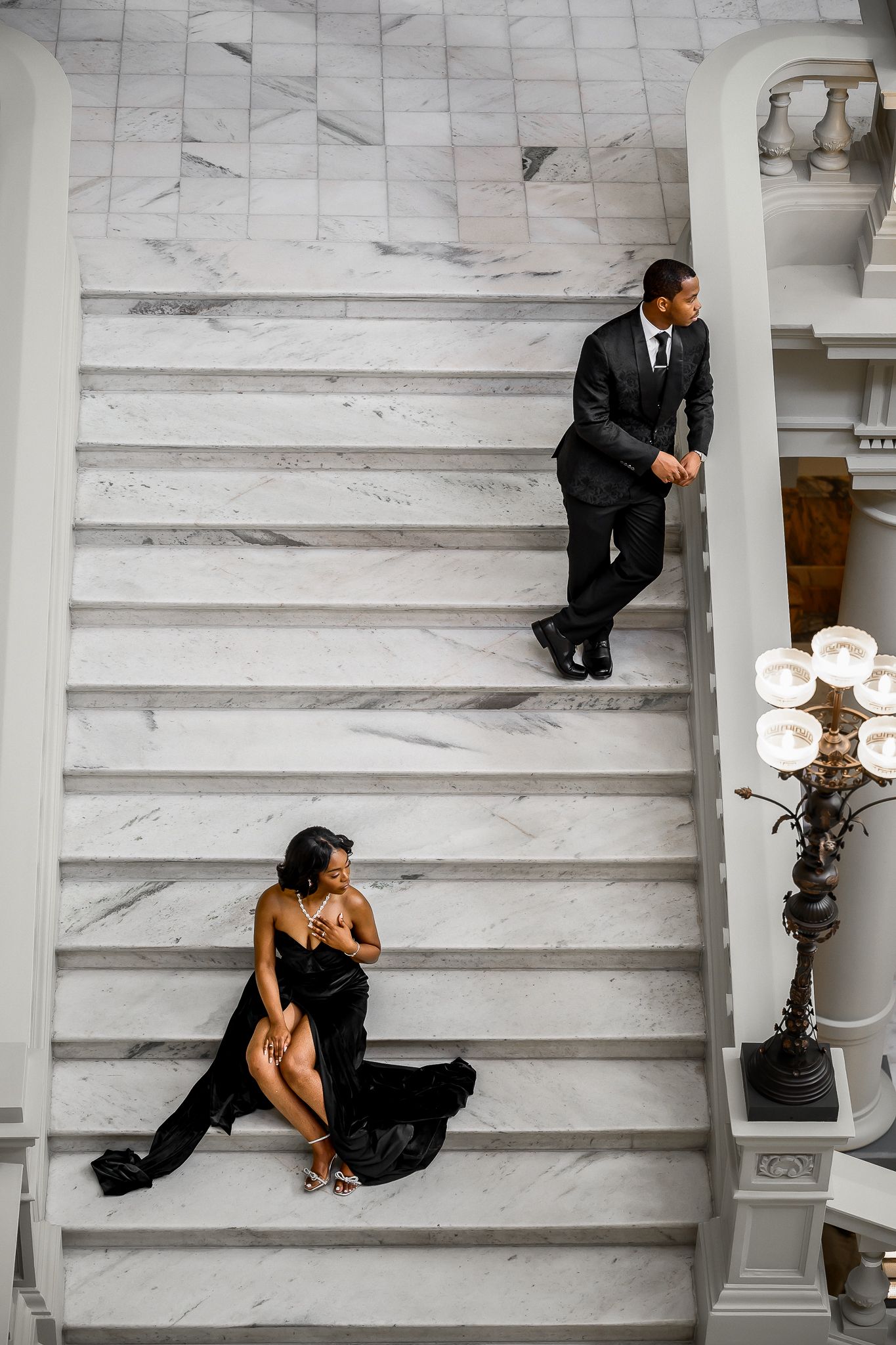 Stylish couple posing on marble steps in a grand building with white columns.