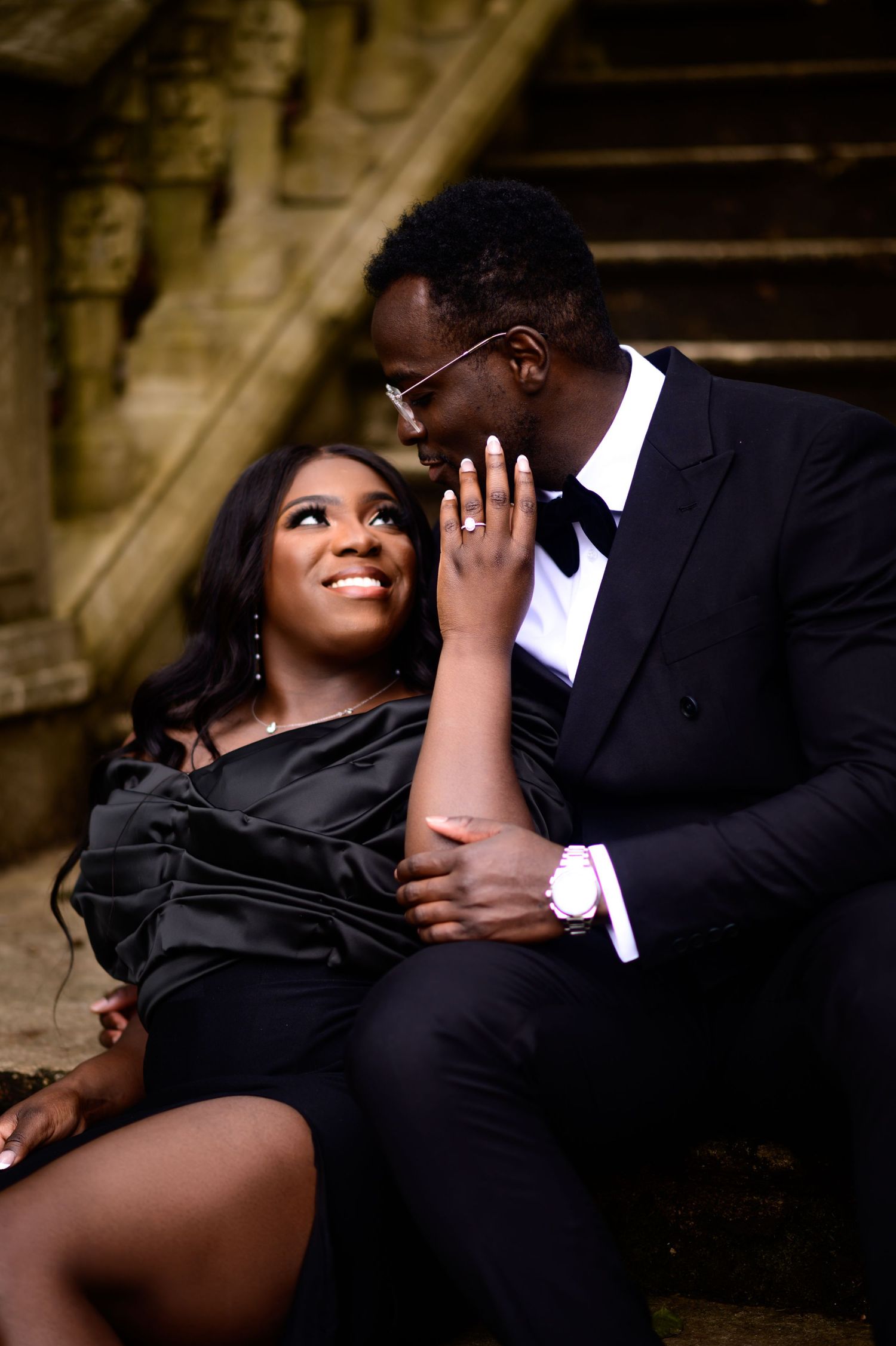 Couple sharing intimate moment on vintage stone staircase in formal evening wear.