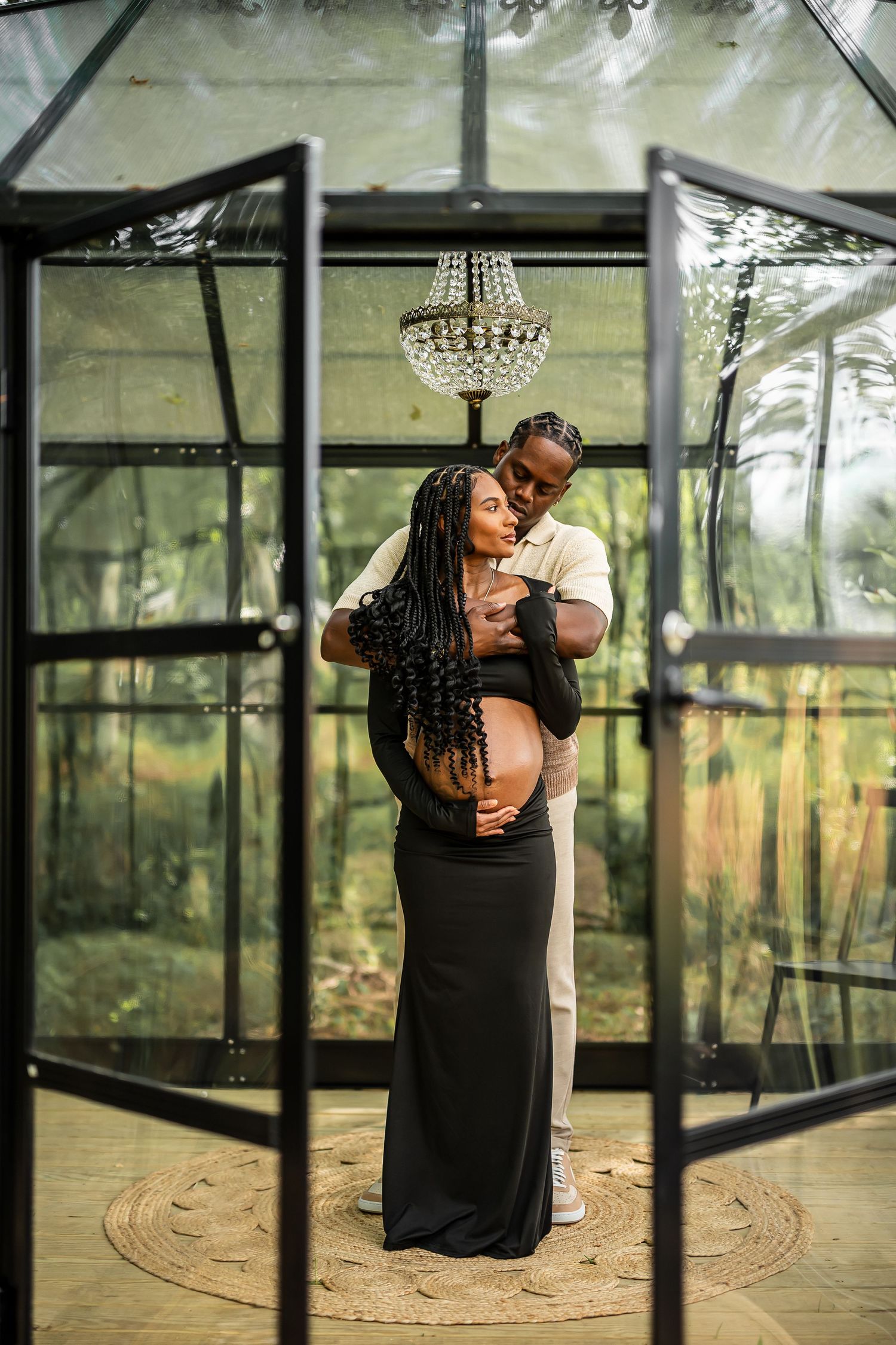 A romantic photoshoot in a glass greenhouse with a chandelier creating an ethereal atmosphere.