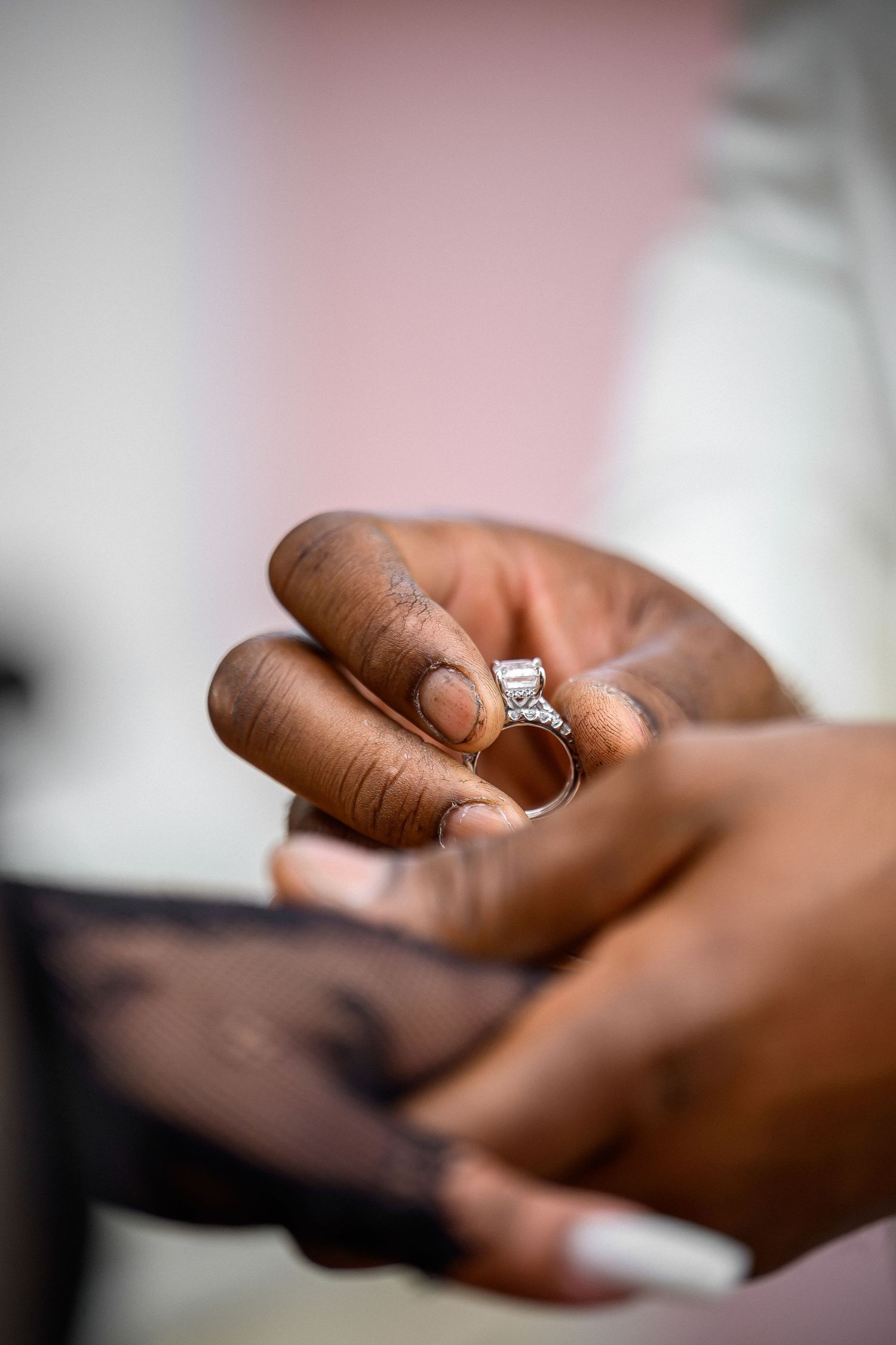 Close-up view of hands holding a sparkling diamond engagement ring against a soft blurred background.