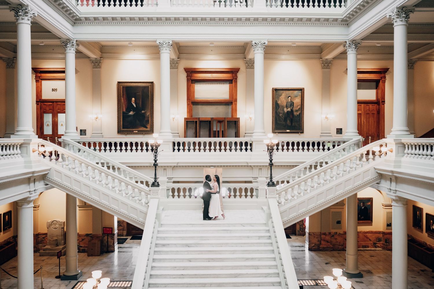 Elegant white marble interior with sweeping staircases and classical columns in symmetrical composition.